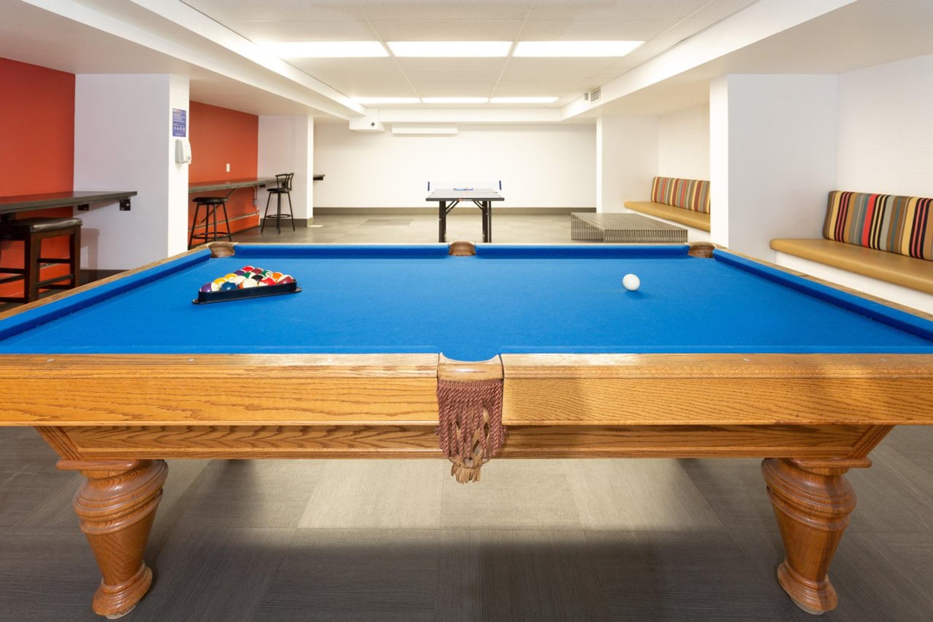 Games room at with full-size pool table, blue felt, striped cushioned seating, ping pong table.