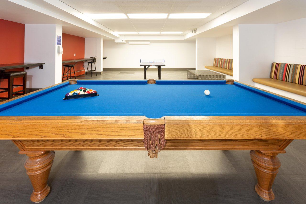 Games room at with full-size pool table, blue felt, striped cushioned seating, ping pong table.