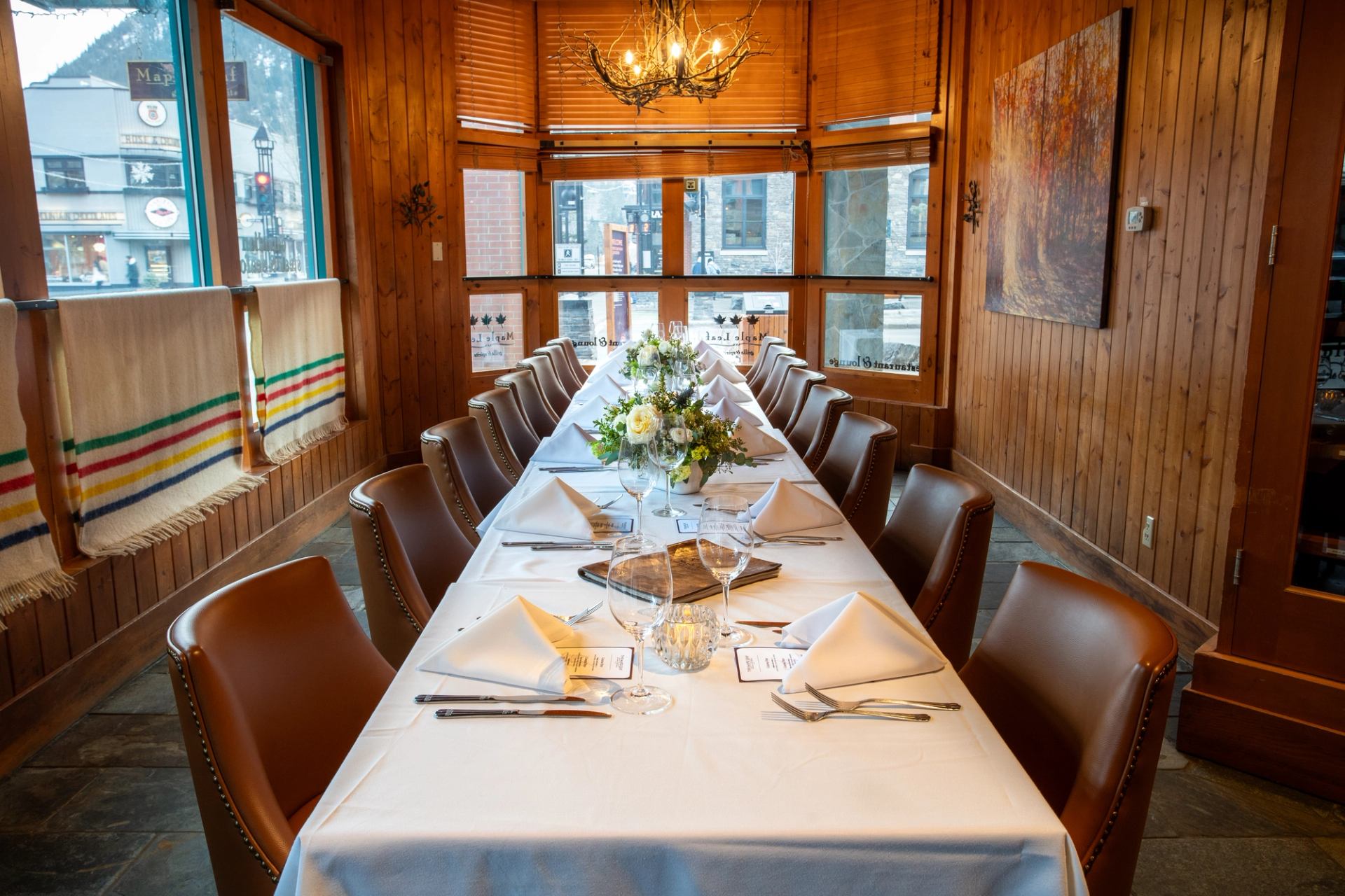 A long table with fourteen seats, white linen table settings and flower vases in a warm wood room