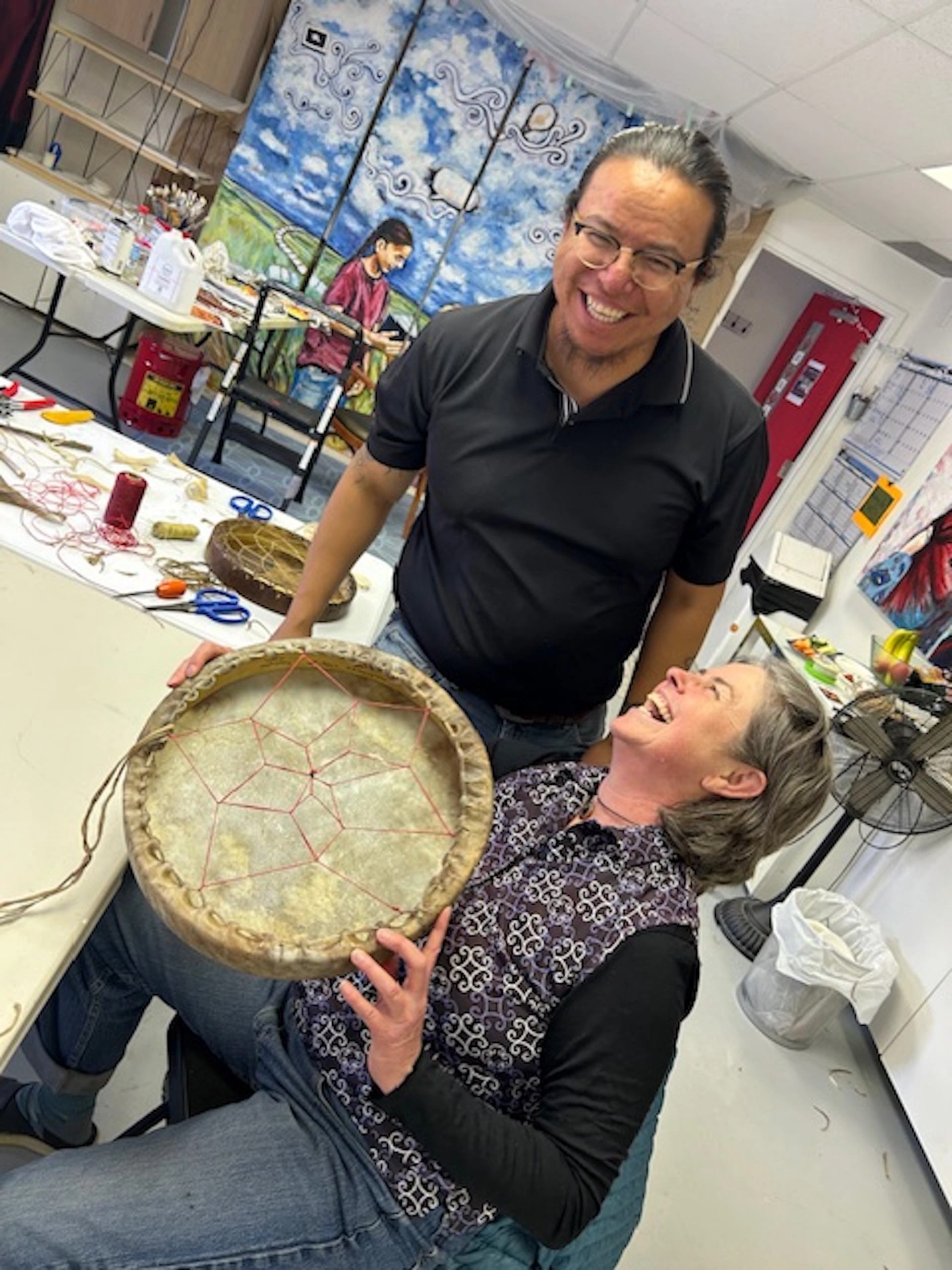Two people in workshop holding circular object, possibly a drum frame.