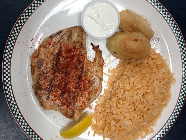 Grilled chicken with rice, potatoes, lemon, and tzatziki sauce on a plate.