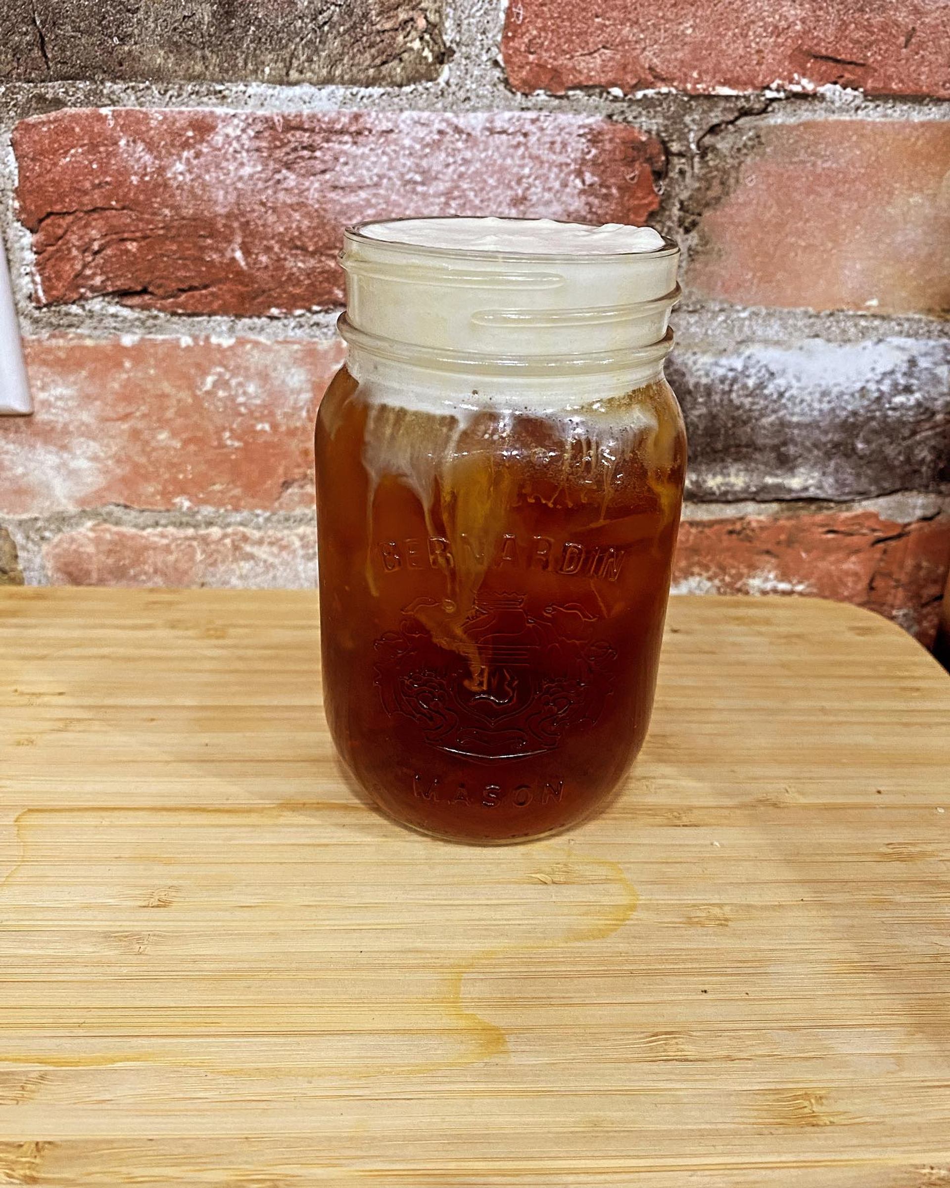 Mason jar with iced coffee or tea and foam on wooden surface, brick wall background at Farmstead Market & More Bistro.