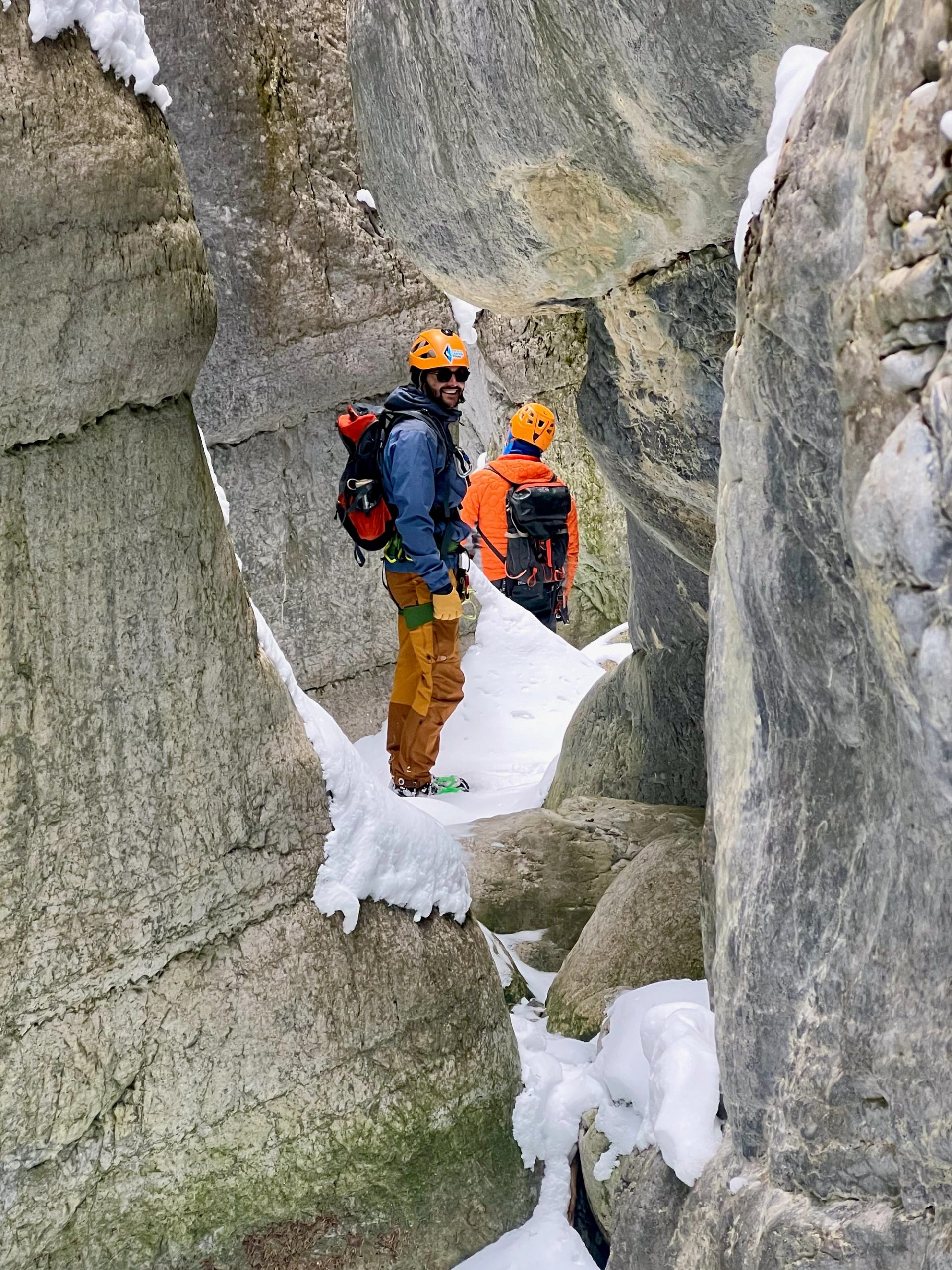 Participants standing on snow adjusting ropes at the base of a rocky cliff.