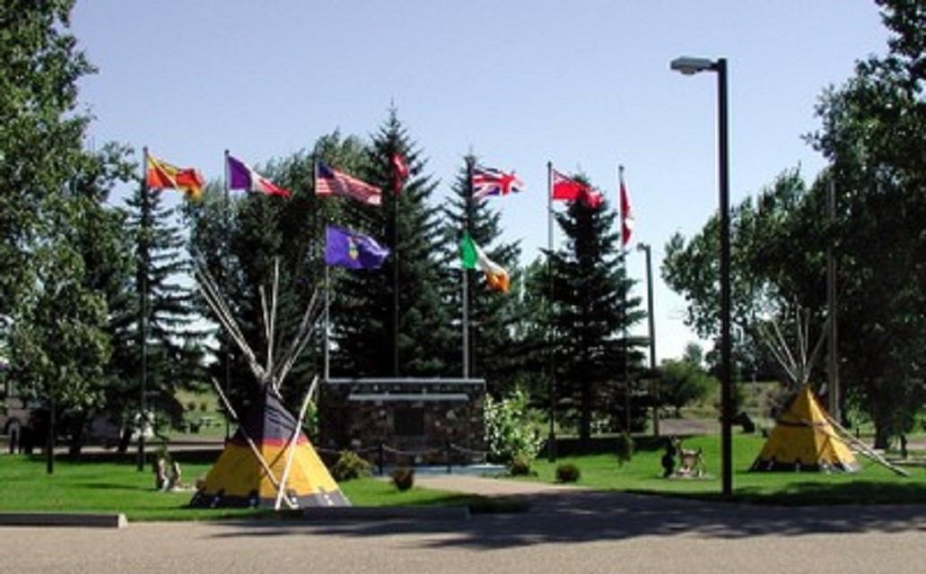 Campground entrance with teepees, tall trees, and eight flags displayed on poles.