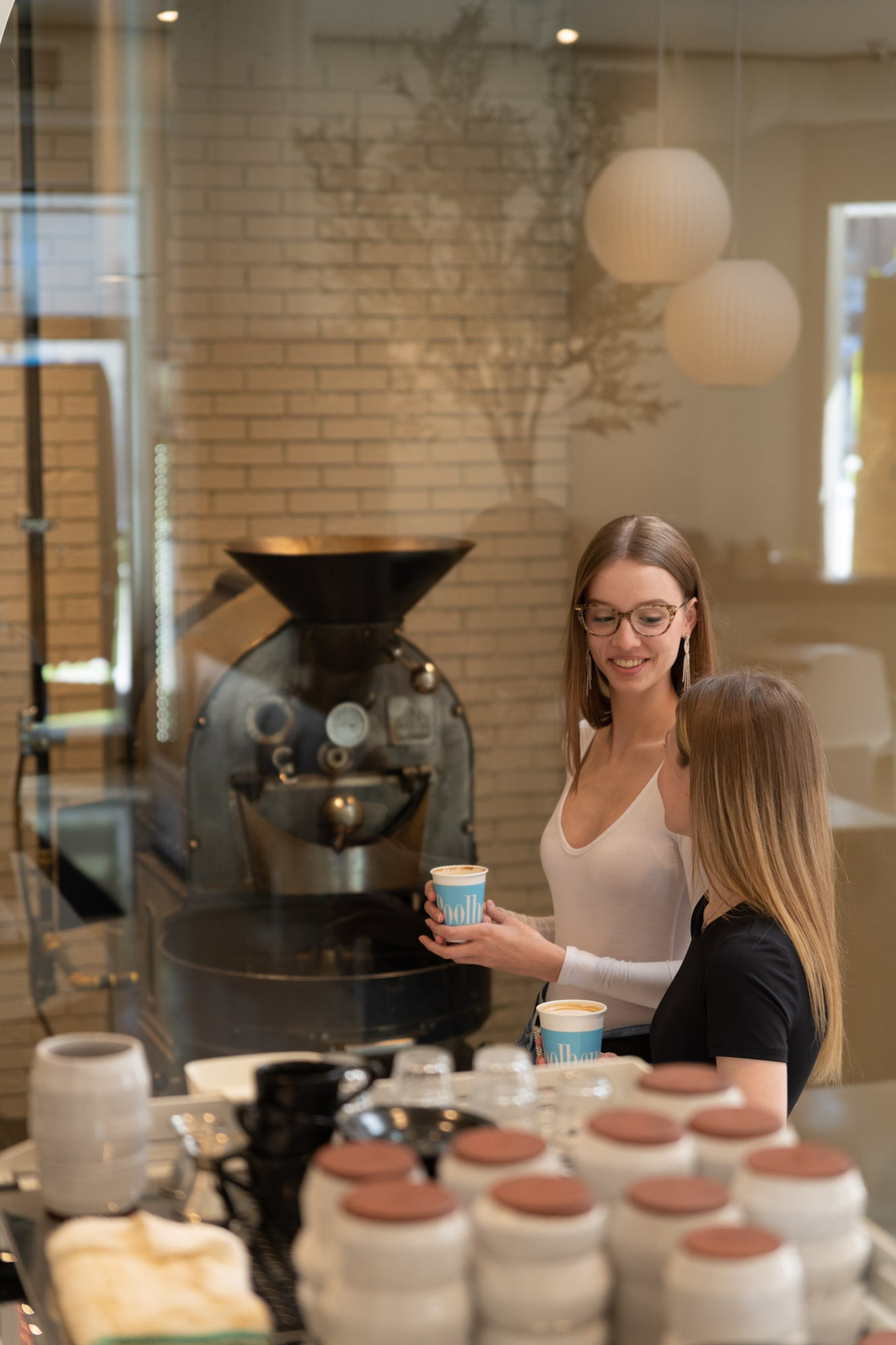 Two people holding coffee cups in a modern café near a large coffee roaster.