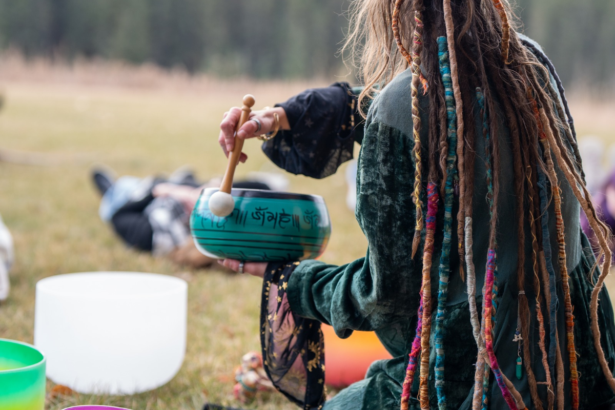 Person plays green singing bowl during outdoor group wellness session.