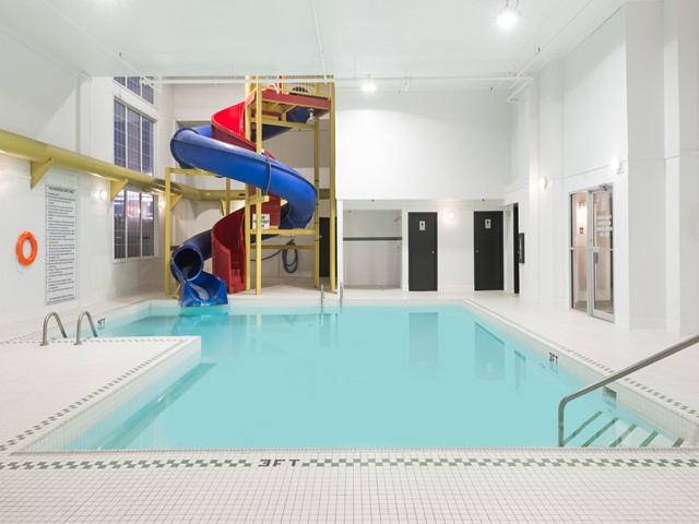 Indoor swimming pool with blue waterslide, tiled deck, ladders and changing room doors.