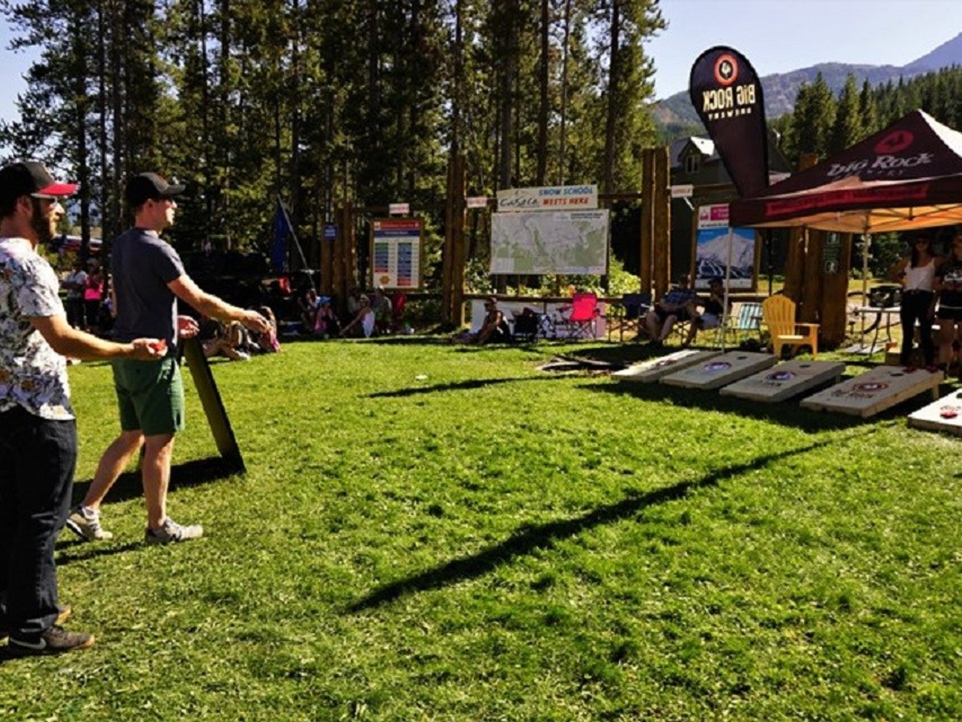 People play bean bag toss on grass near Big Rock Brewing tent and trees.