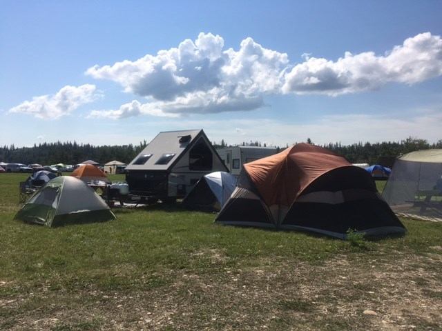Campsite with tents and trailer on grassy field at Métis Crossing Campground.