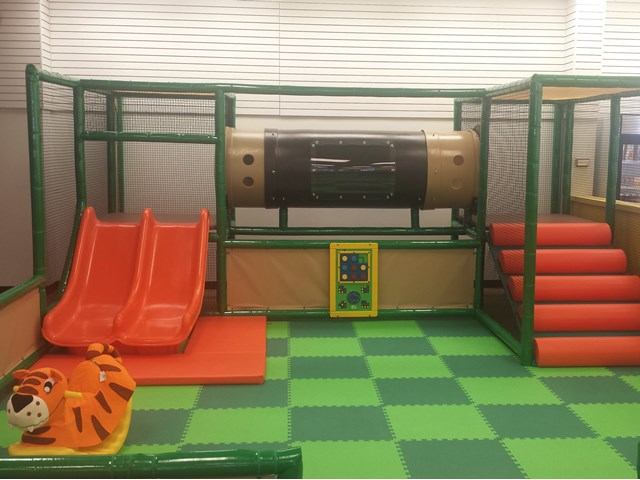 Indoor soft play area with orange slides, padded steps, tunnel and tiger ride-on toy.