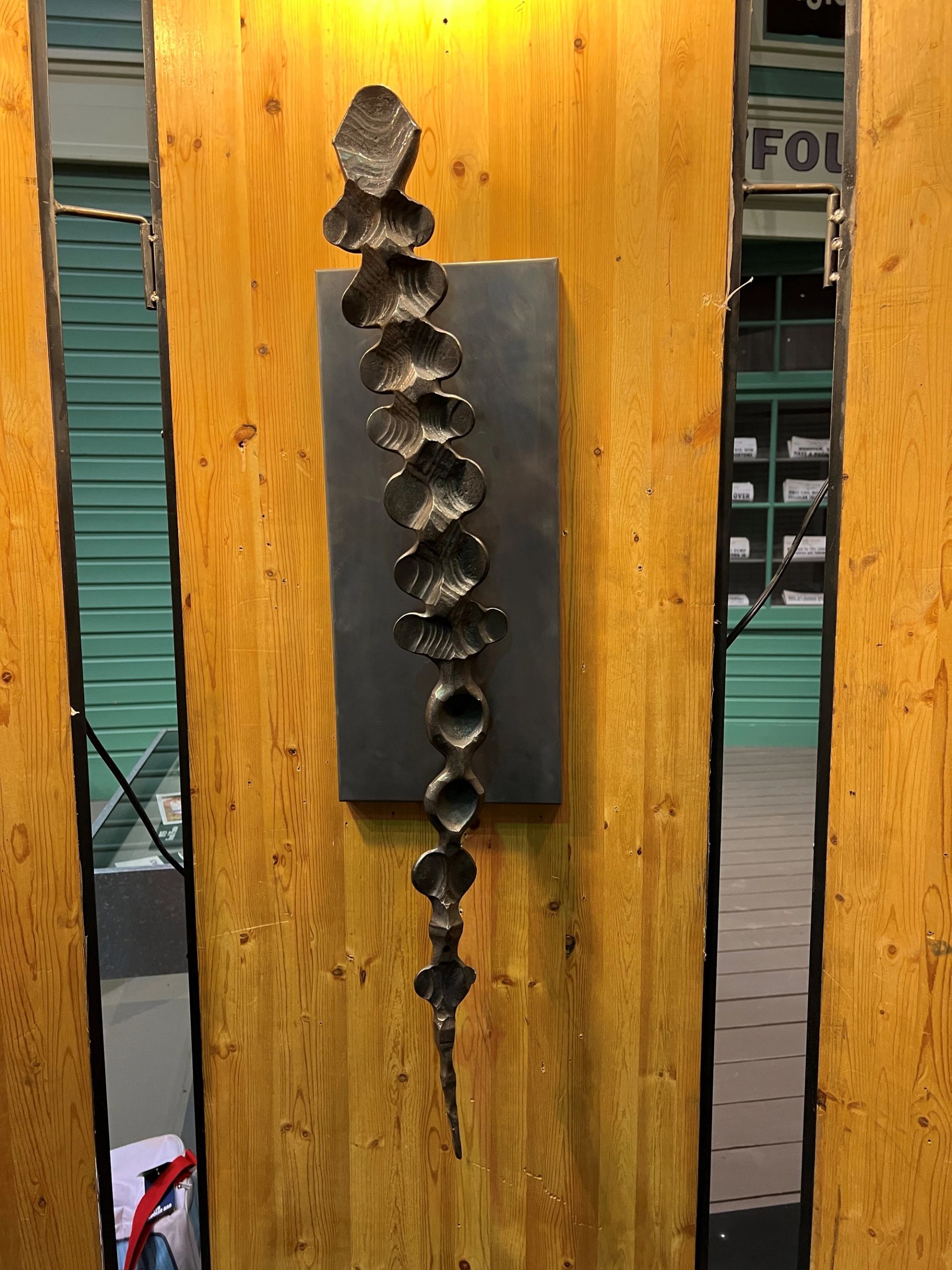 Abstract metal wall sculpture mounted on wood panel with grey backing.