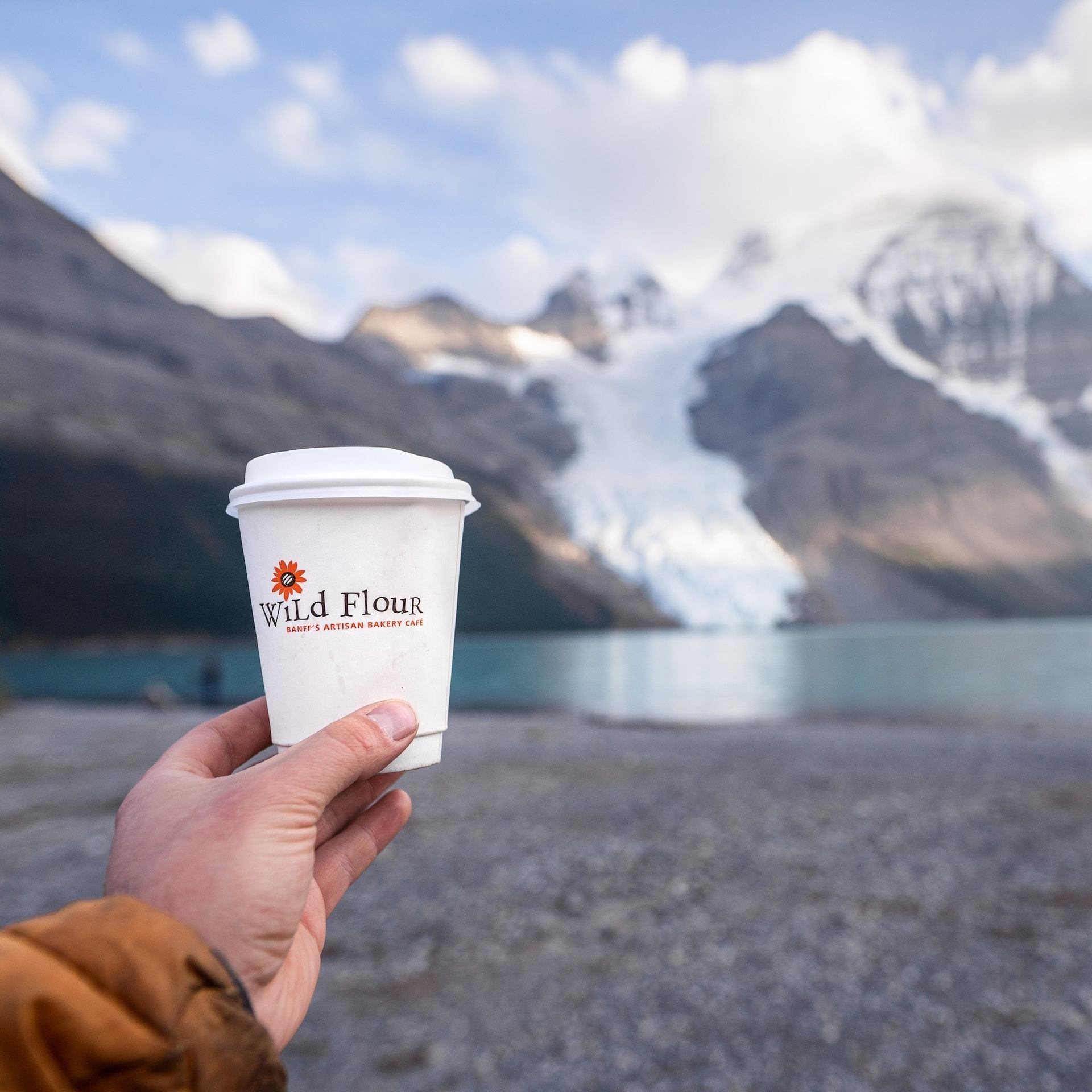 Wild Flour coffee cup held with a stunning glacier and mountain backdrop.
