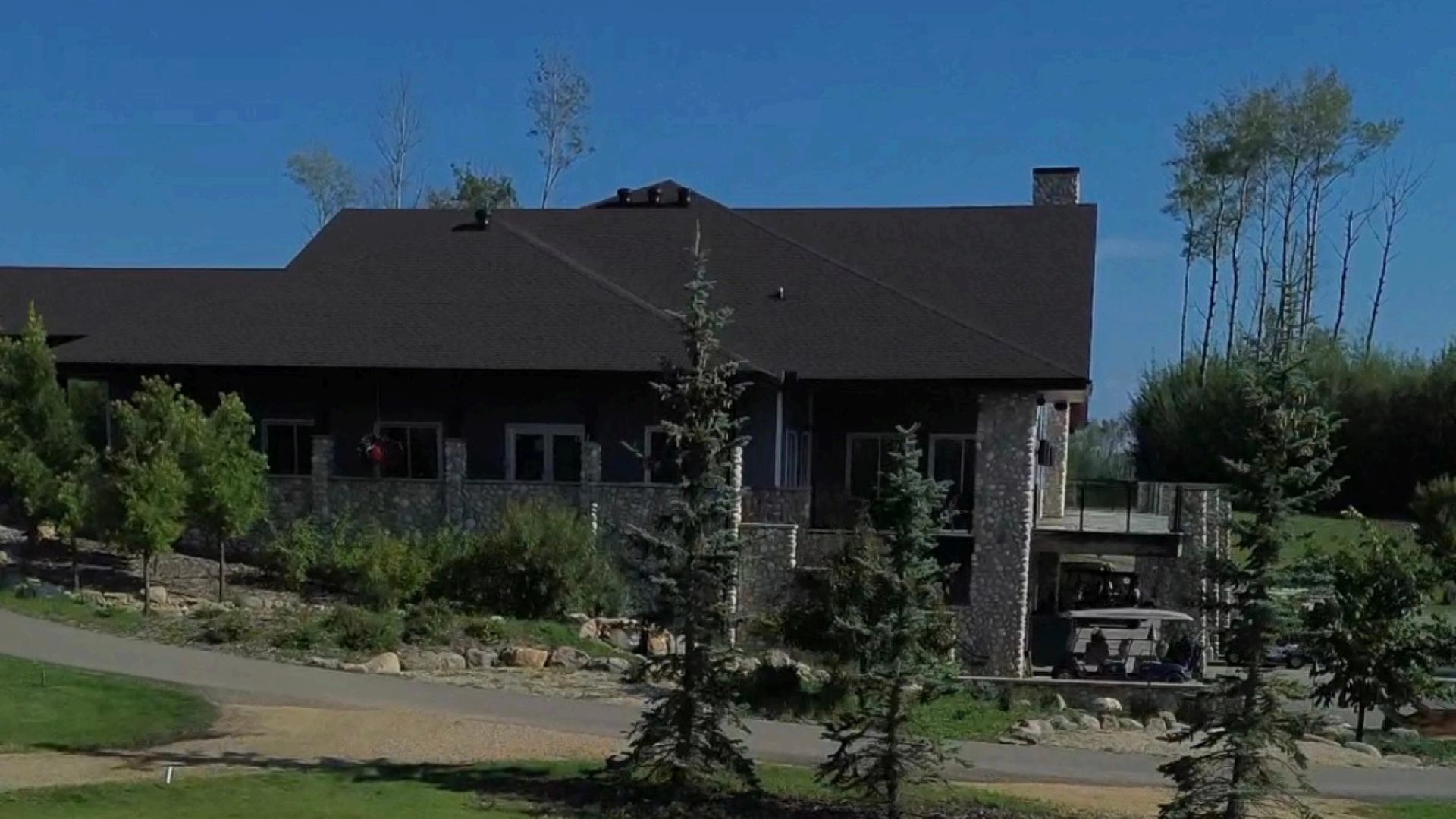 Stone lodge with a dark roof, surrounded by evergreen trees and landscaped grounds.