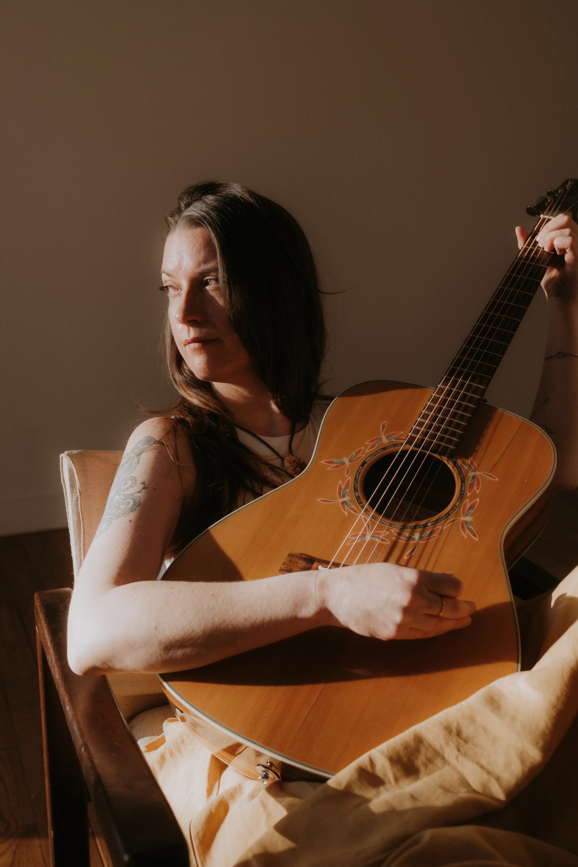 Person sitting in warm light, holding an acoustic guitar with floral soundhole design.