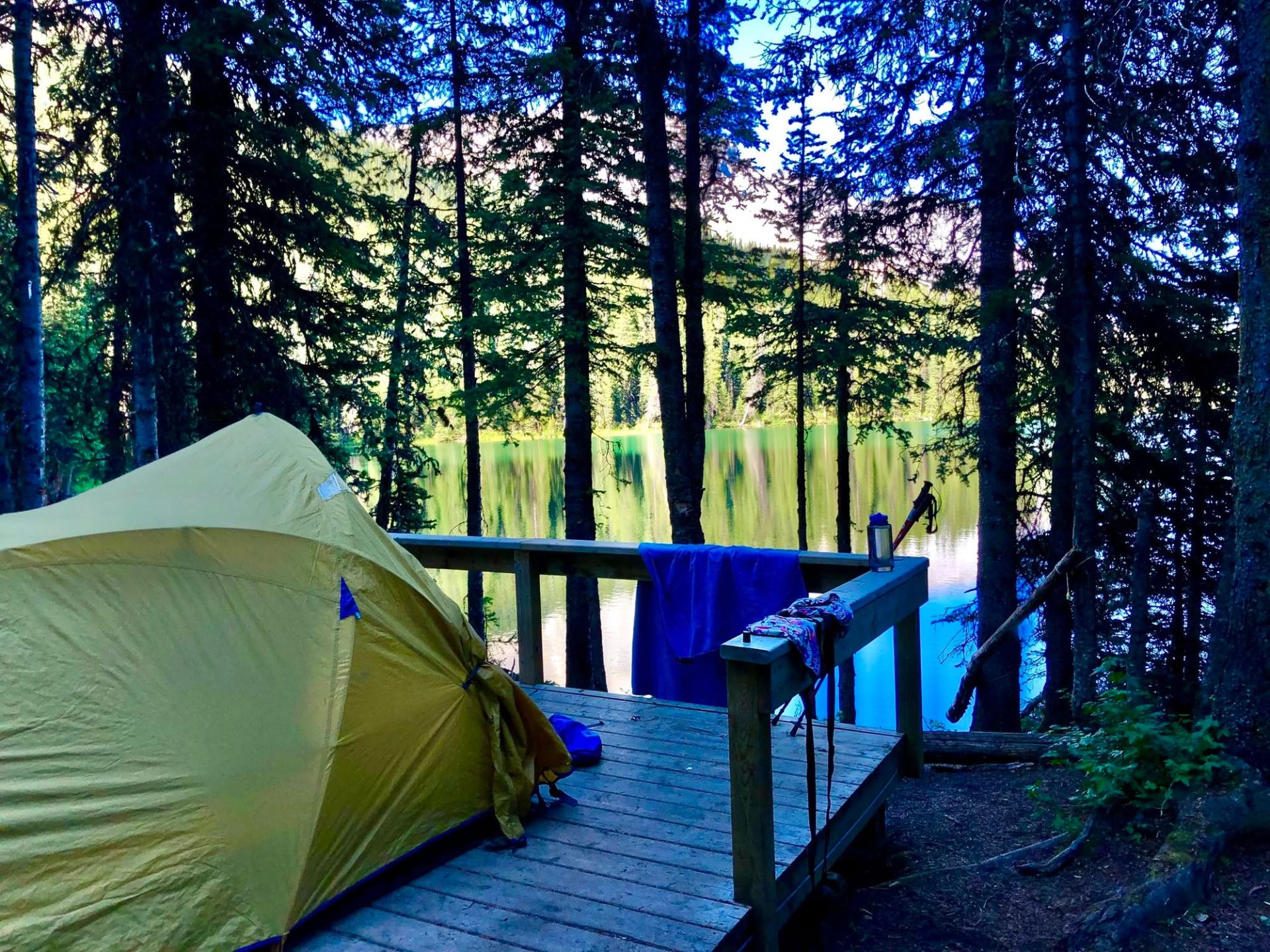 Yellow tent on a wooden platform overlooking a forest lake.