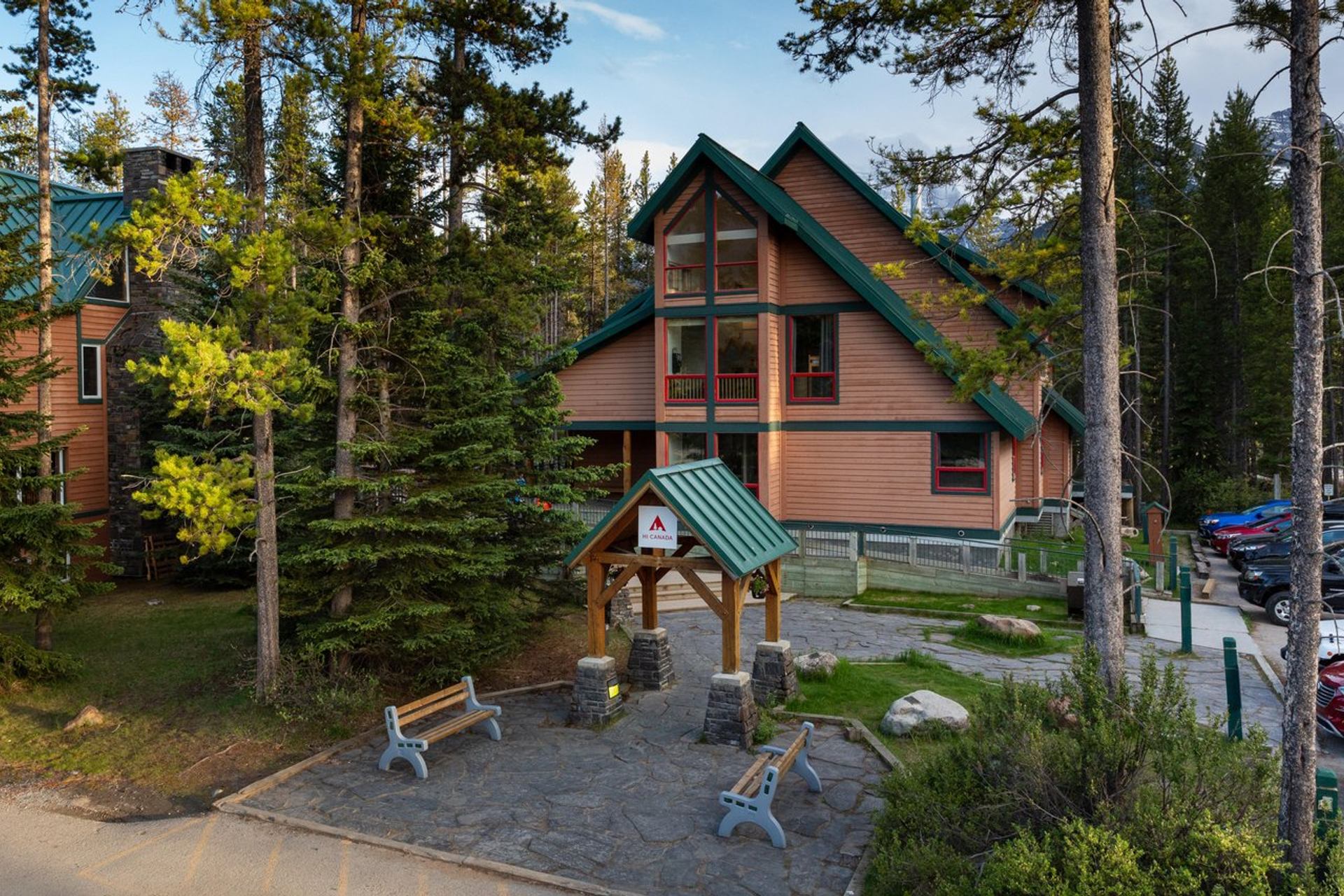 Lodge-style building with green roof and balconies in a forested mountain setting.