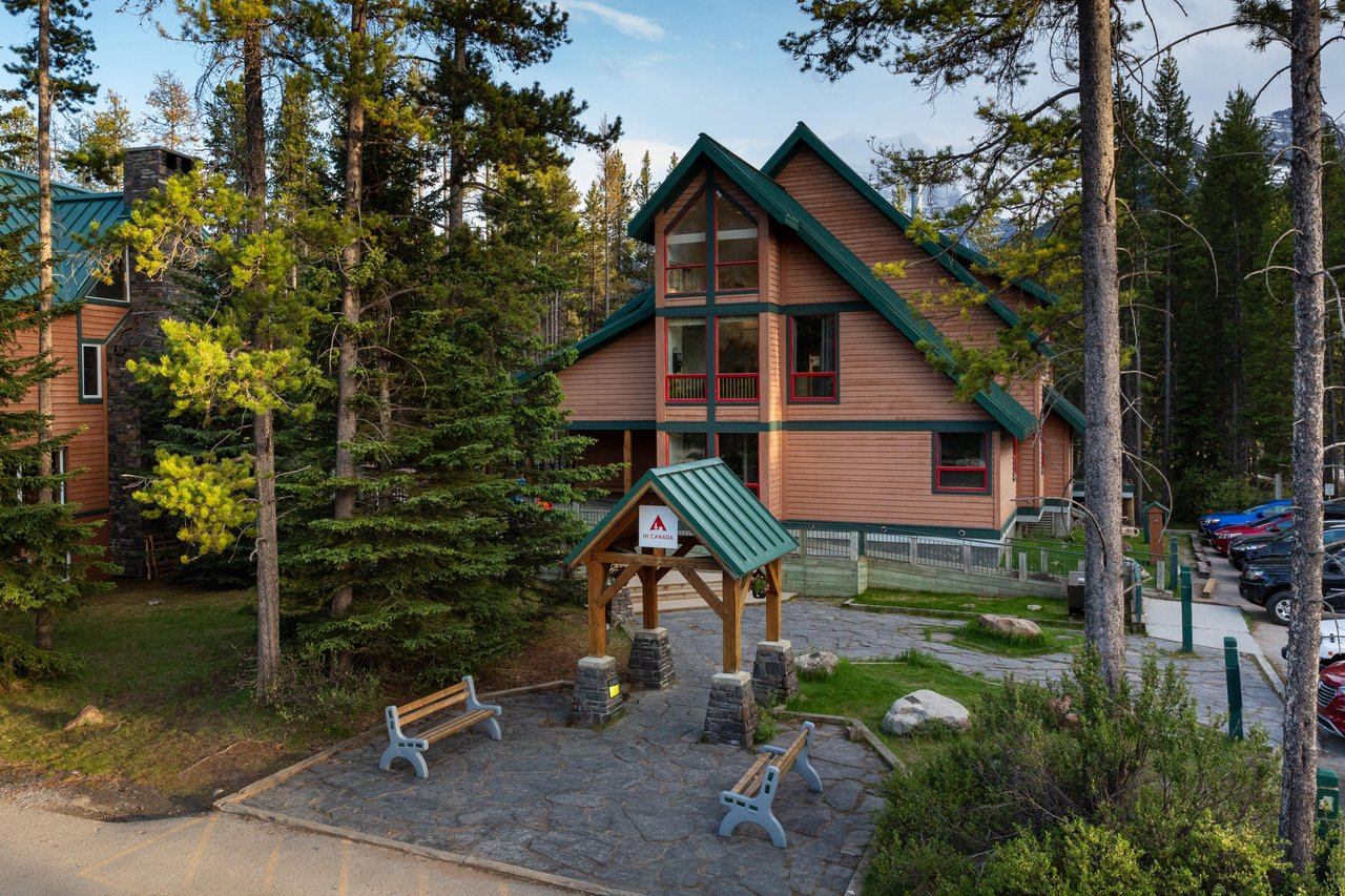 Lodge-style building with green roof and balconies in a forested mountain setting.
