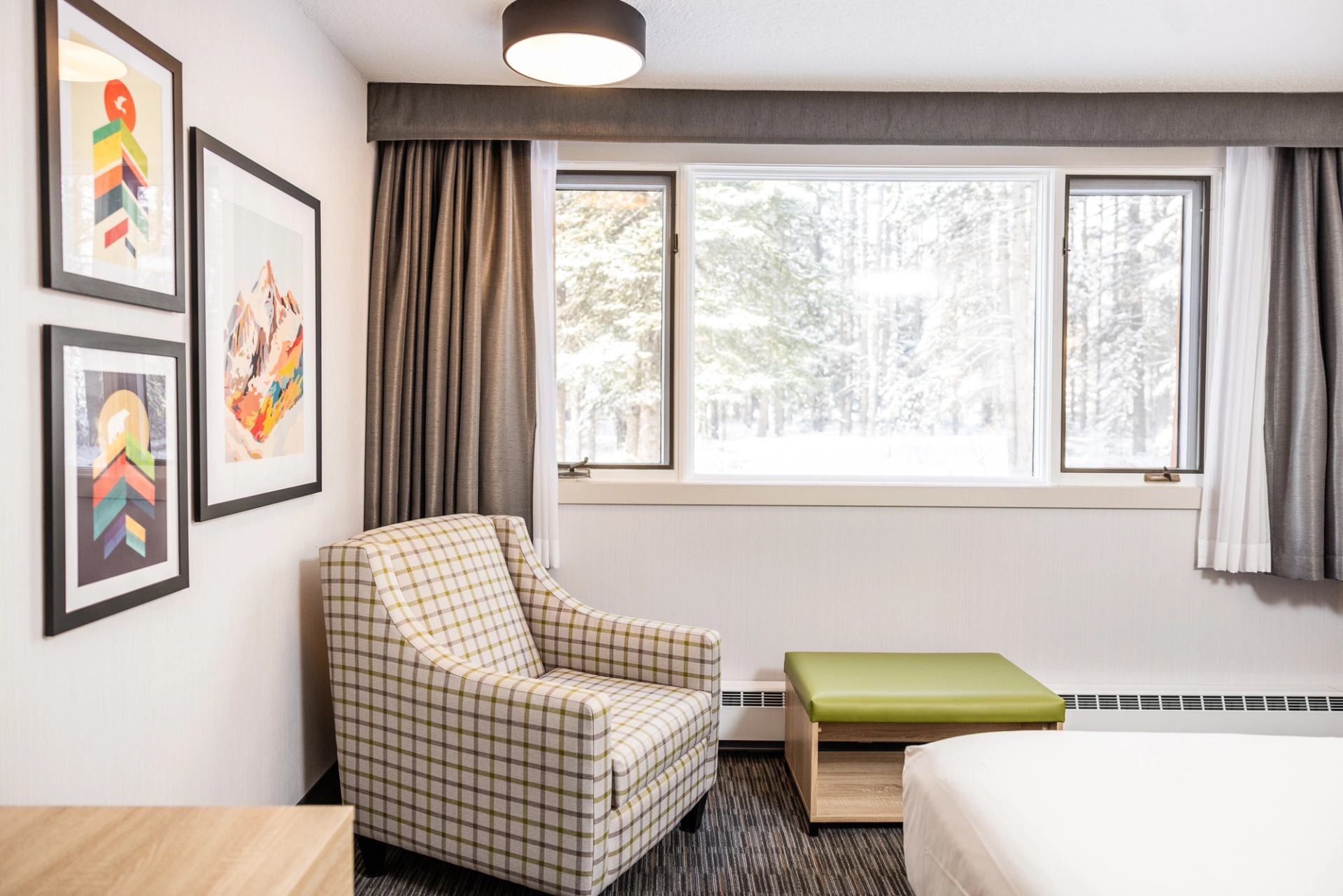 Bright lodge room with a plaid armchair, green ottoman, and large window view.