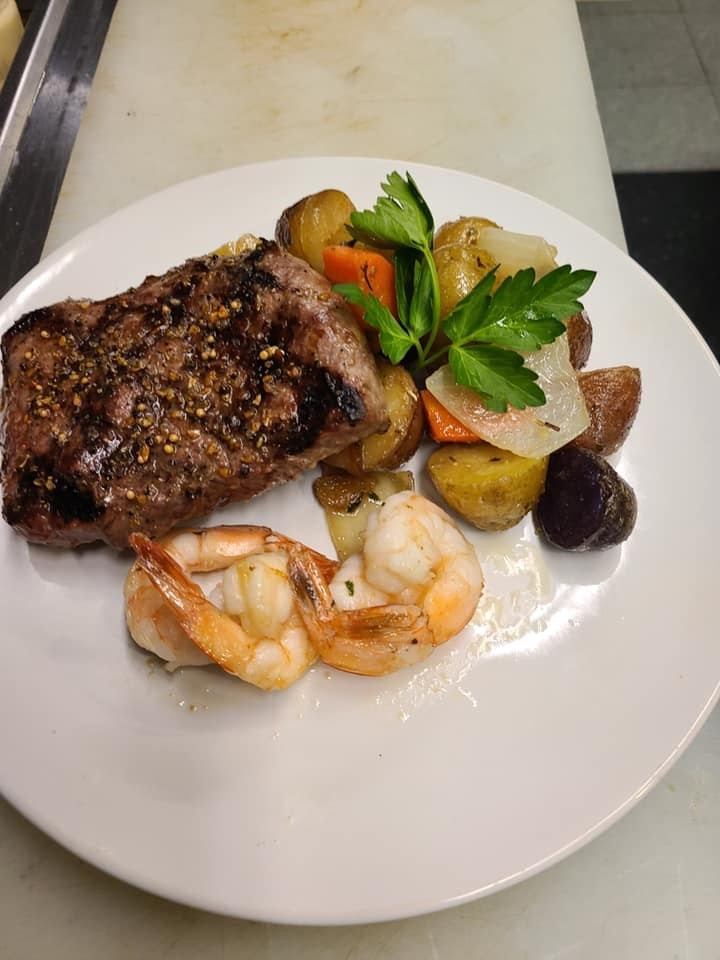 Grilled steak with shrimp and roasted vegetables on a white plate.