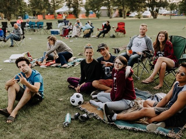 Backyard festival crowd sitting on grass with camping chairs and a soccer ball.