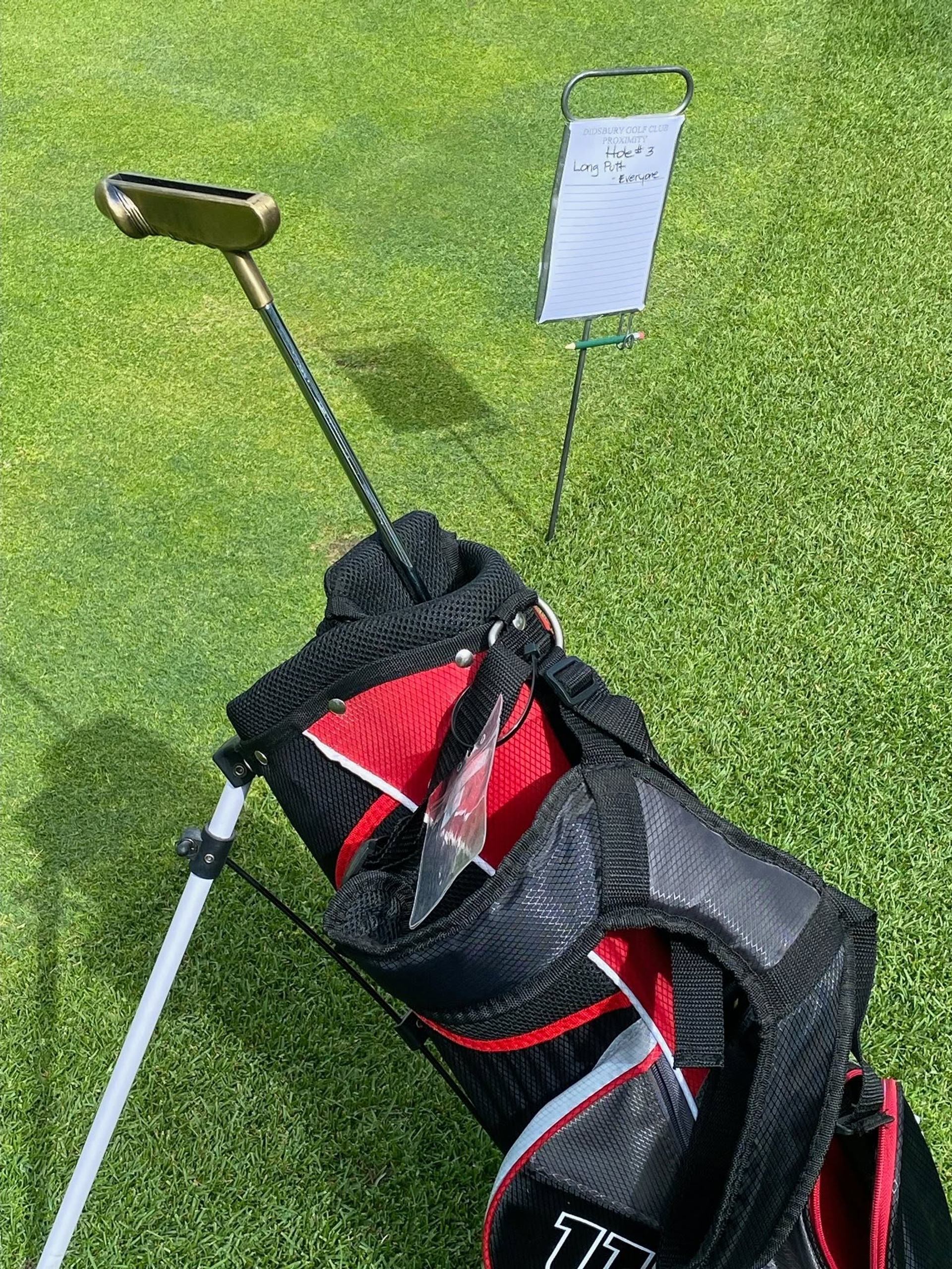 Golf bag with putter on green beside clipboard sign for long putt contest.