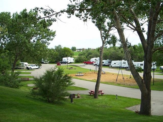An RV campground with several recreational vehicles, a playground, green trees, and paved roads.