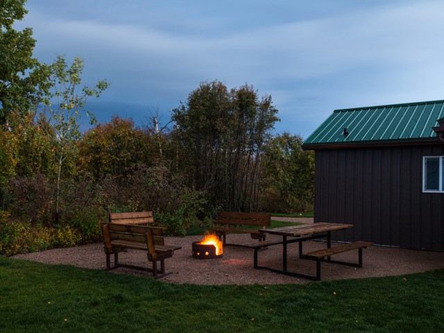 Outside the cabin at nighttime with a fire, chairs and picnic table.