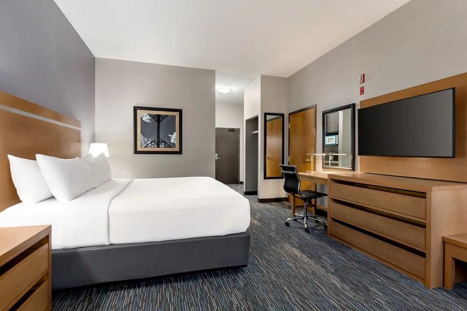 Modern guest room with king bed, work desk, and flat-screen TV at Wingate by Wyndham.