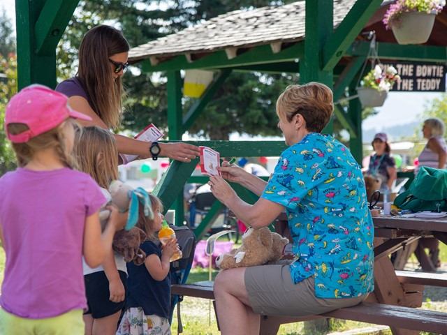 Children watch a woman and man paint bottles at an outdoor heritage festival booth.