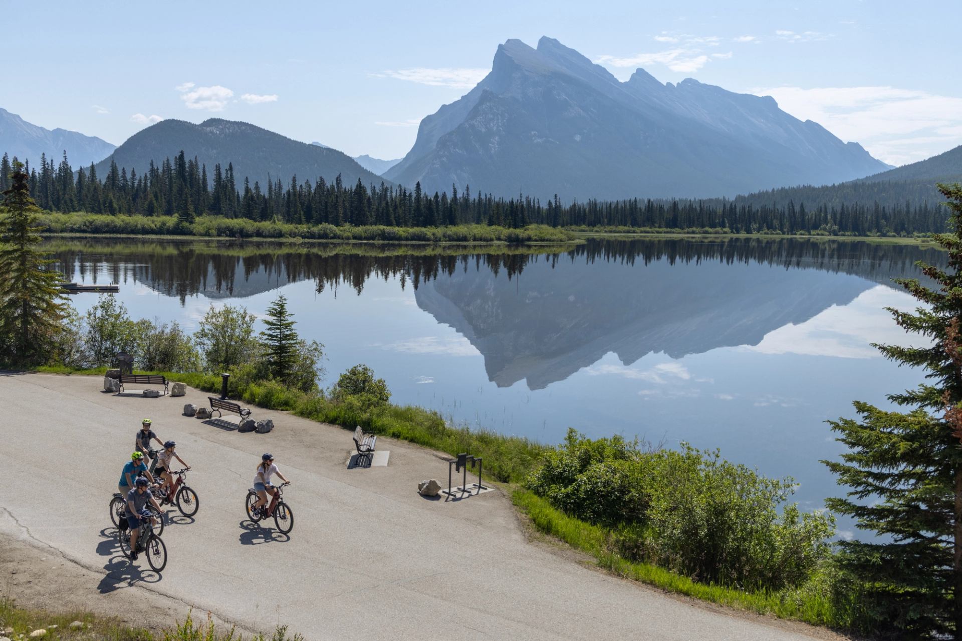 Cyclists ride lakeside trail with mountain views in scenic Banff National Park.