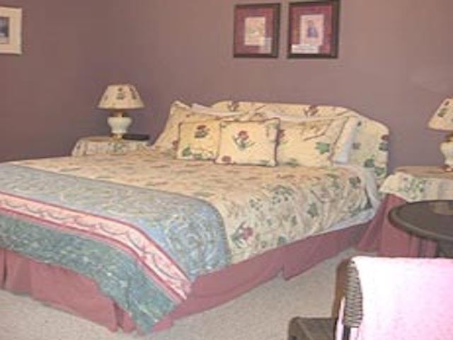 Bedroom bed with patterned quilt, bedside lamps, and framed wall pictures in view.