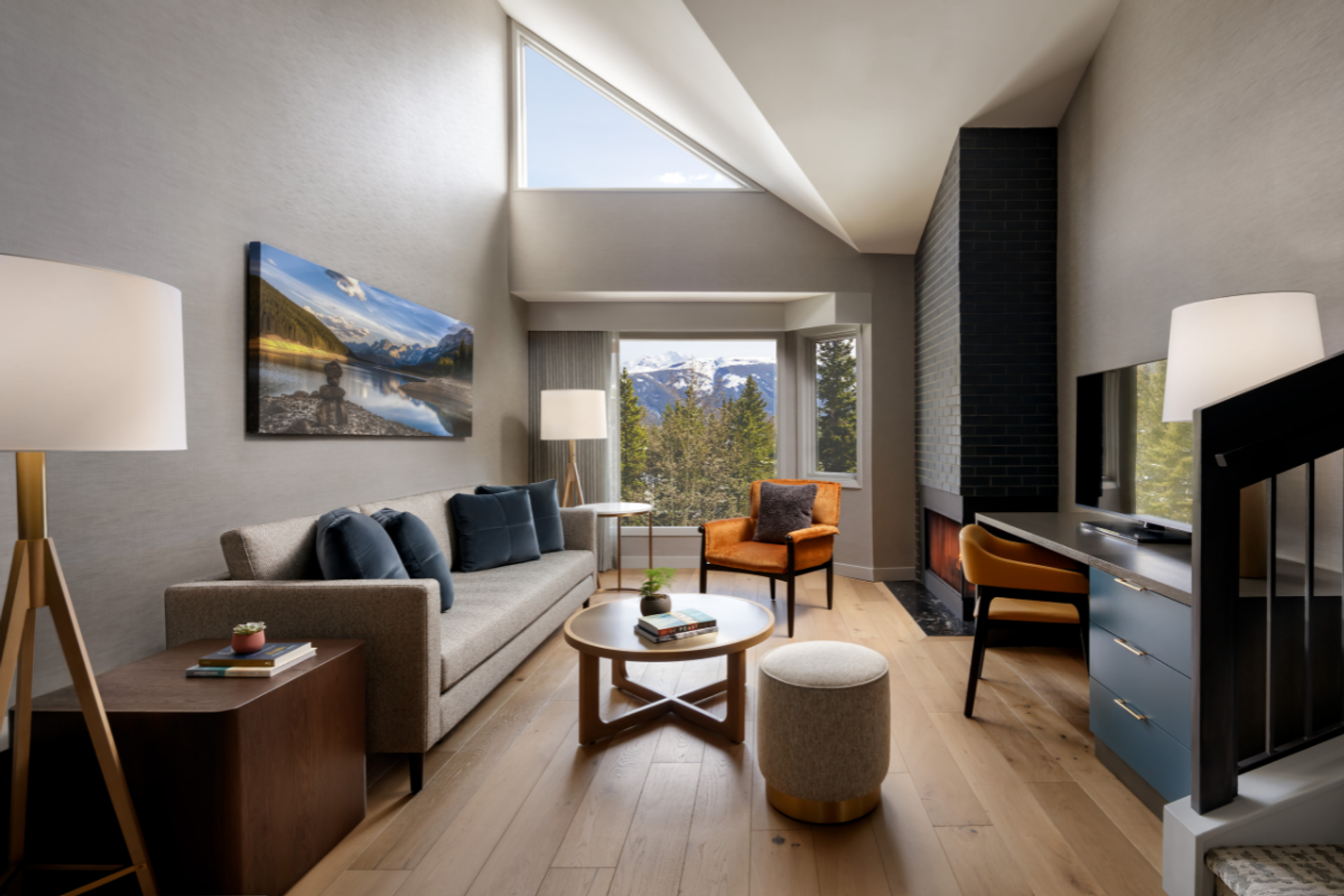 Modern living room with mountain view, sofa, orange chair, fireplace and desk.