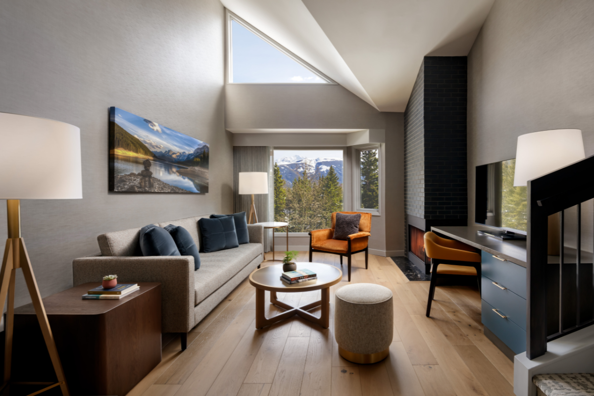 Modern living room with mountain view, sofa, orange chair, fireplace and desk.