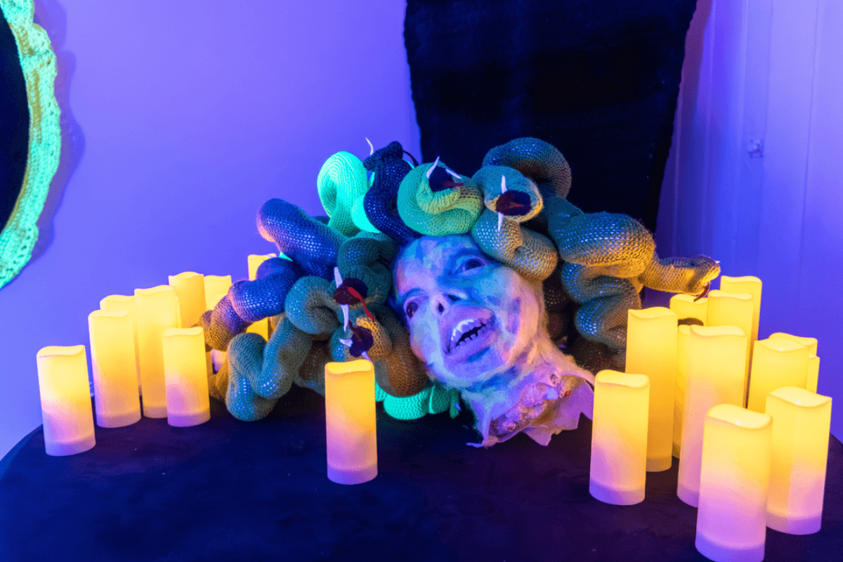 Medusa head prop with snake hair surrounded by glowing candles under purple light.