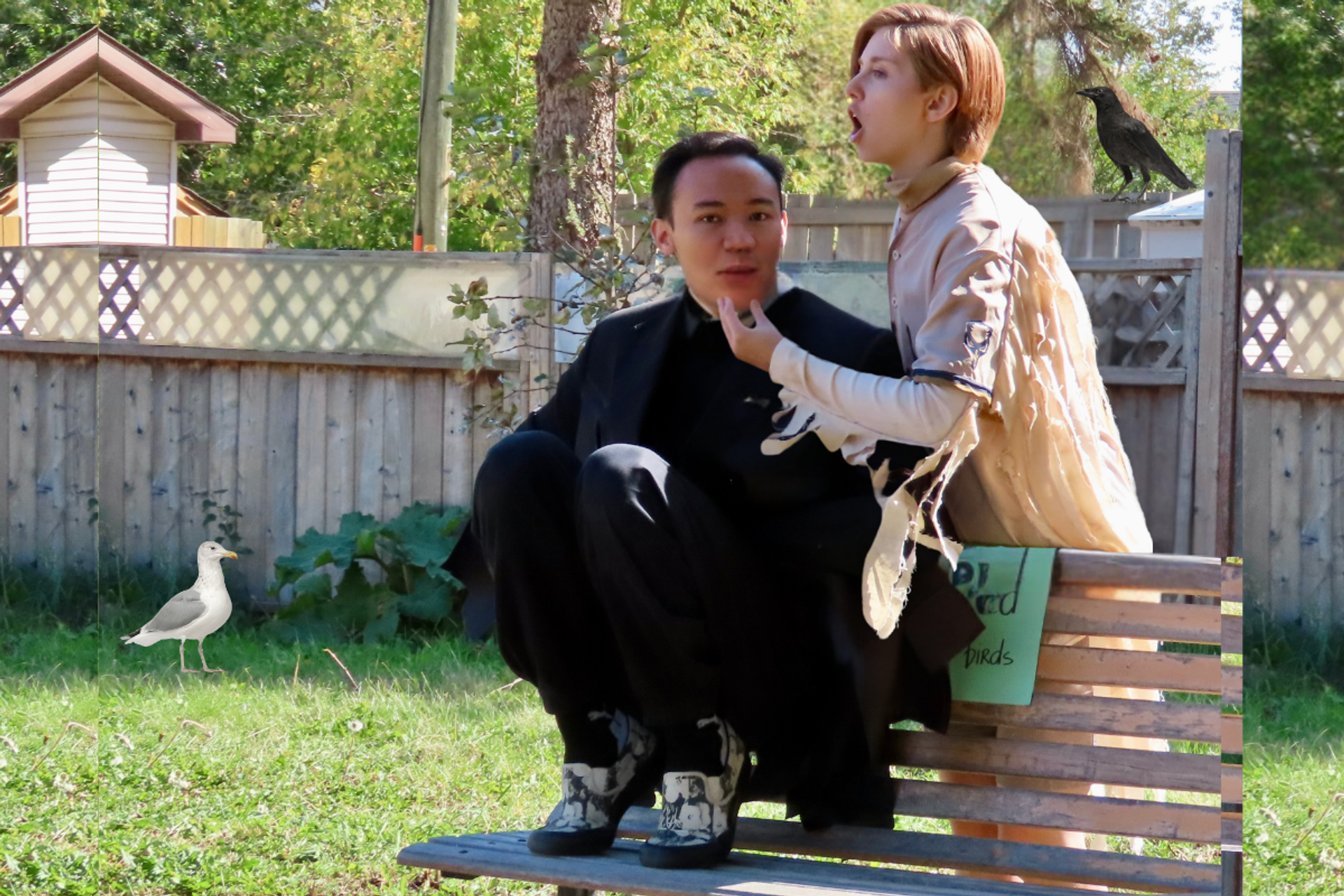 Two people on a wooden bench in a fenced yard with birds nearby.