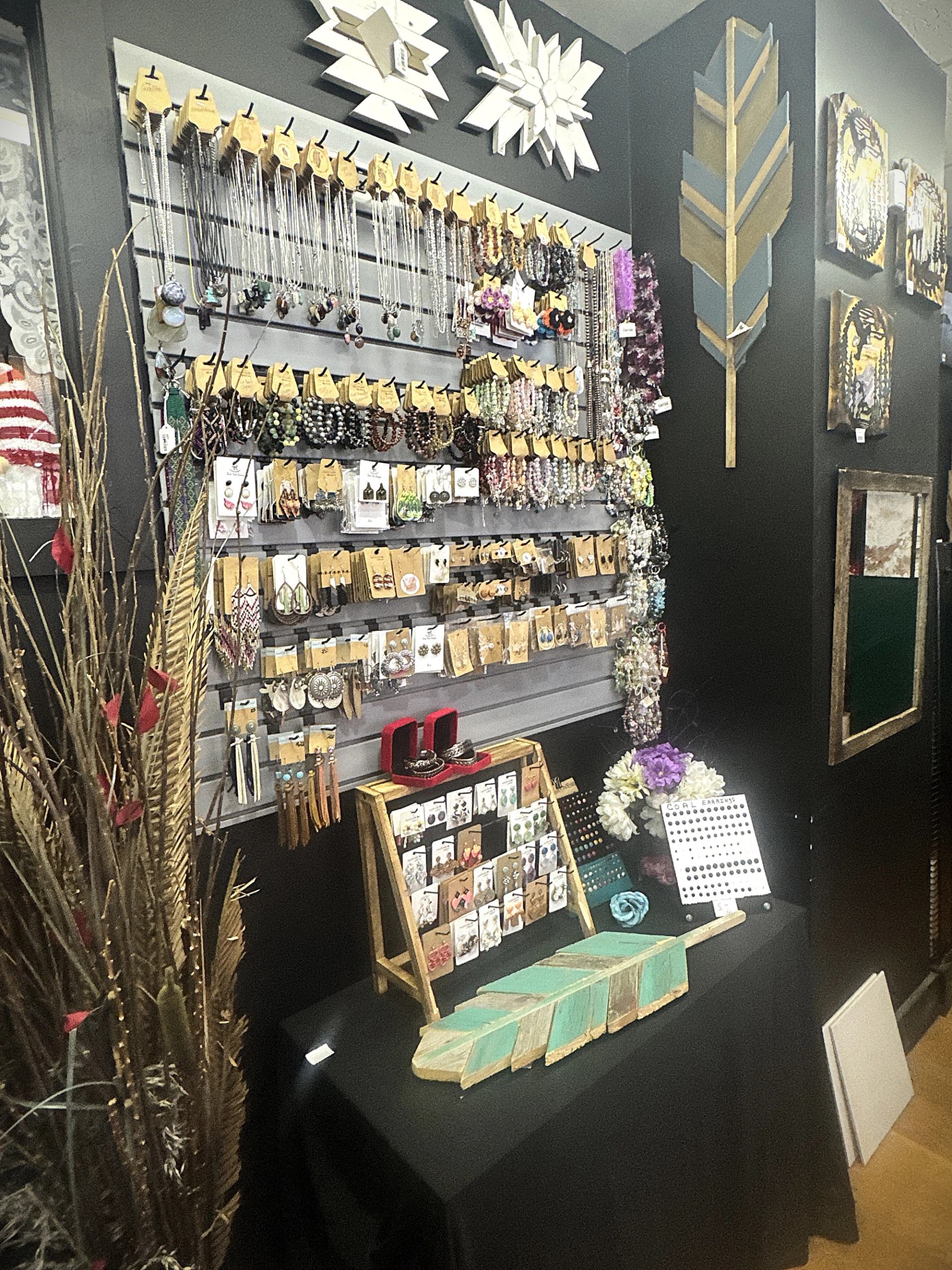 Display of necklaces, earrings, bracelets, and wall décor arranged across shelves and a tabletop.