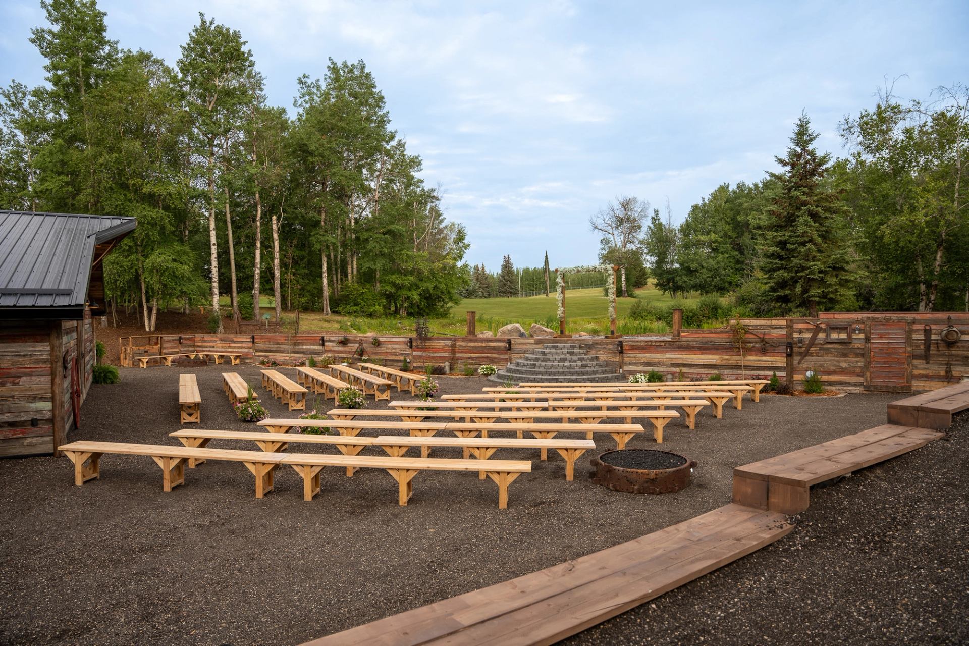 Semi-circle wooden benches in a forested outdoor venue with gravel paths.