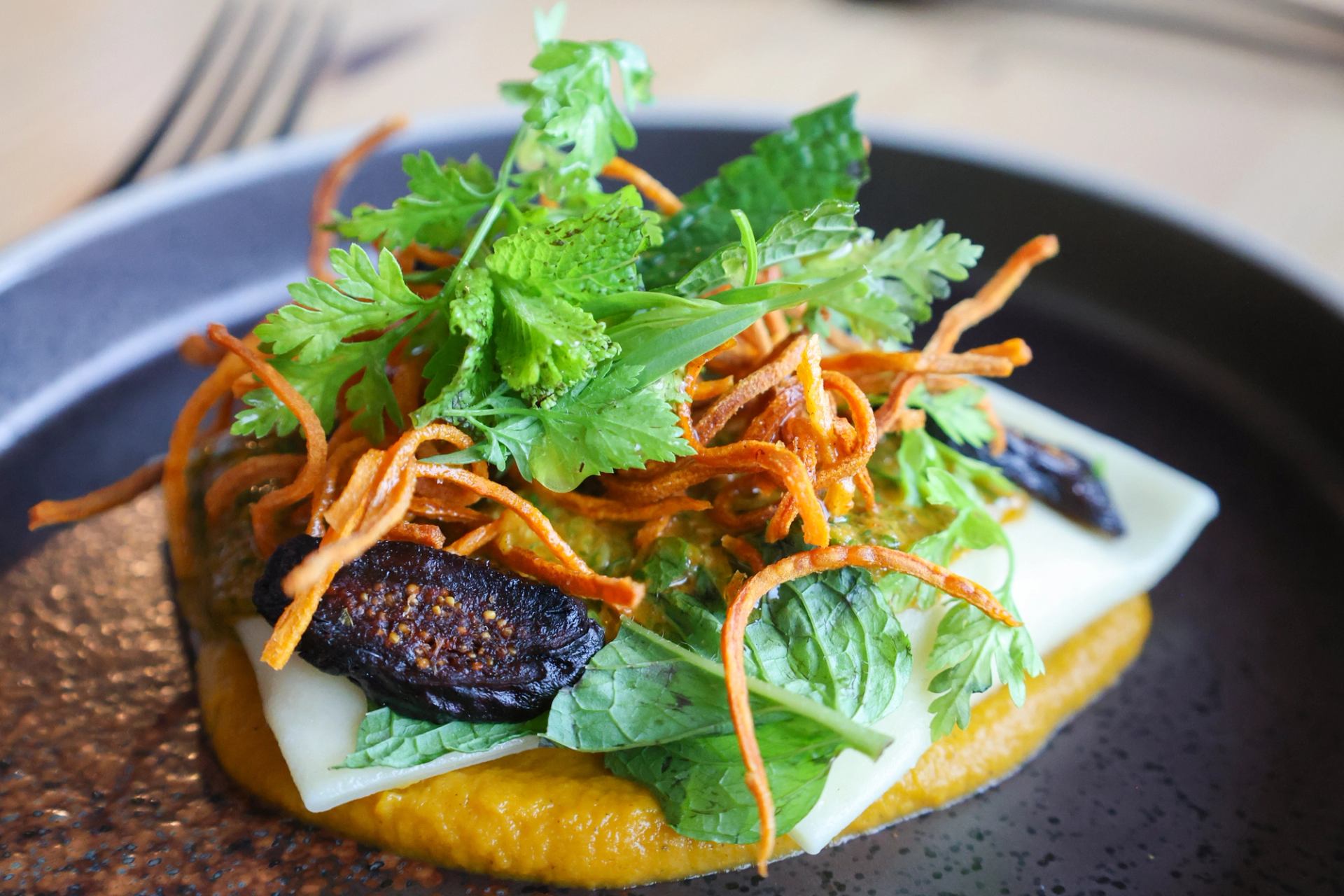Colorful dish with greens, crispy carrot strands, and pasta on a dark plate.