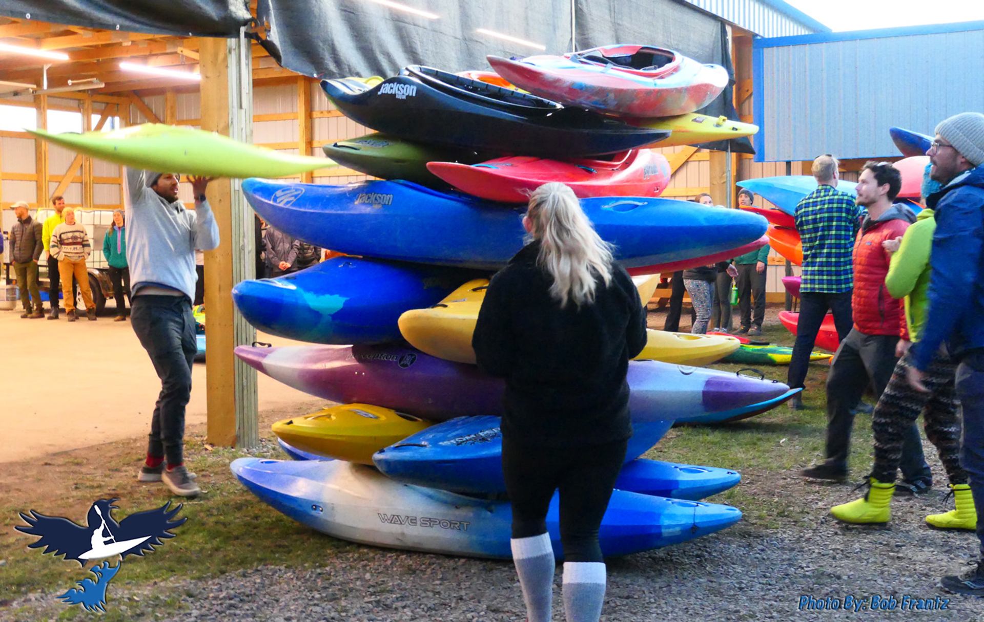 Colorful kayaks stacked outside near a group of people preparing gear.