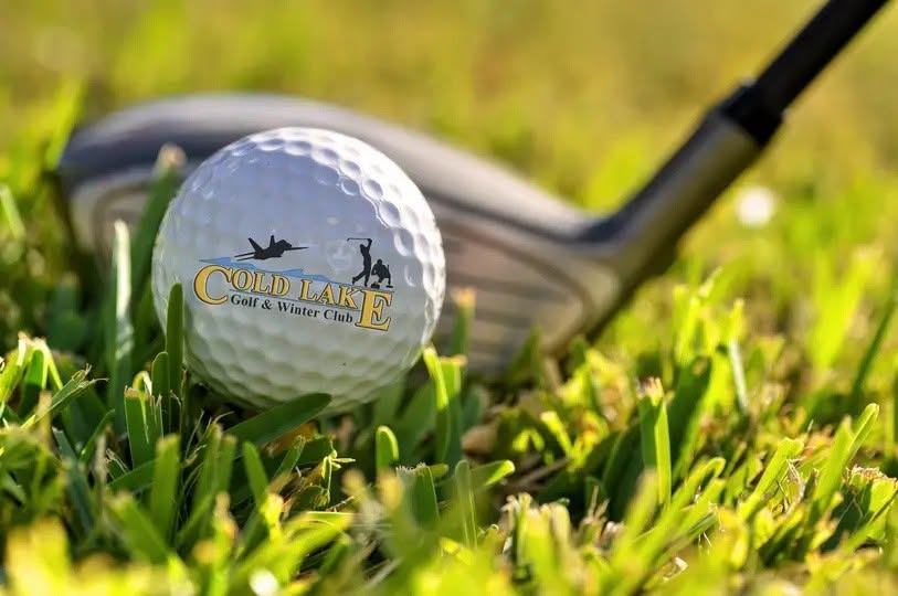Golf ball with Cold Lake Golf and Winter Club logo beside club on grass.