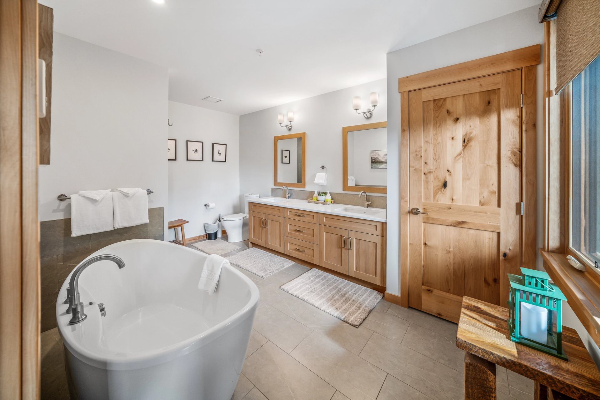 Spacious bathroom with freestanding tub, double vanity, toilet and wooden door under bright lighting.