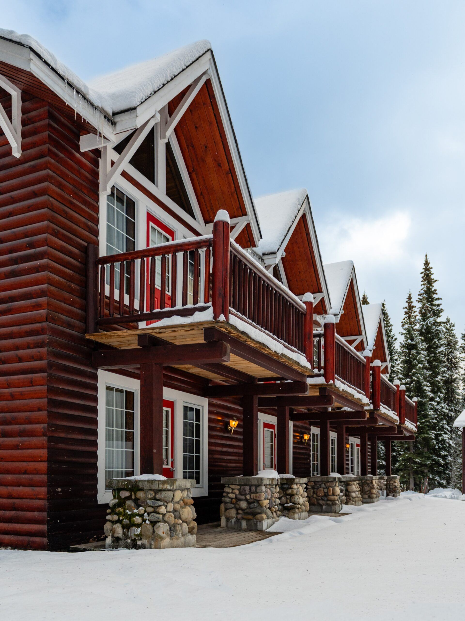 Row of log cabins with balconies covered in snow under cloudy sky