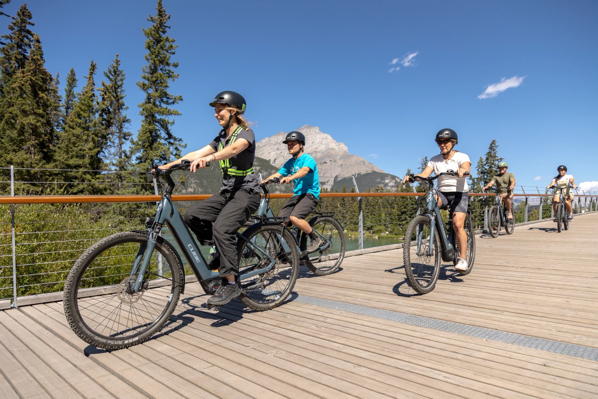 Group riding bikes along a wooden path with mountain views at Banff Adventures.