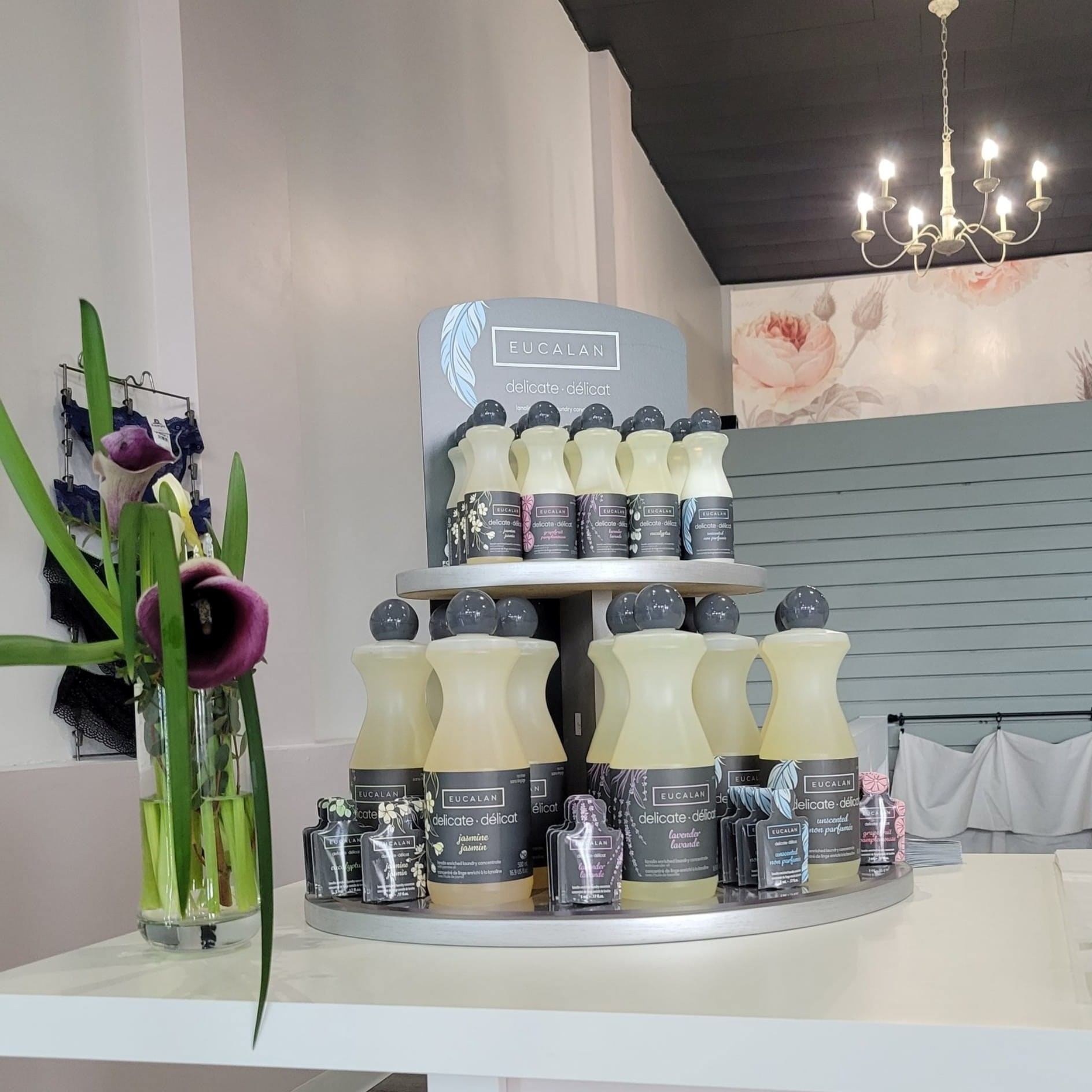 Eucalan retail display with bottles and lotion pumps, chandelier overhead, floral mural backdrop.