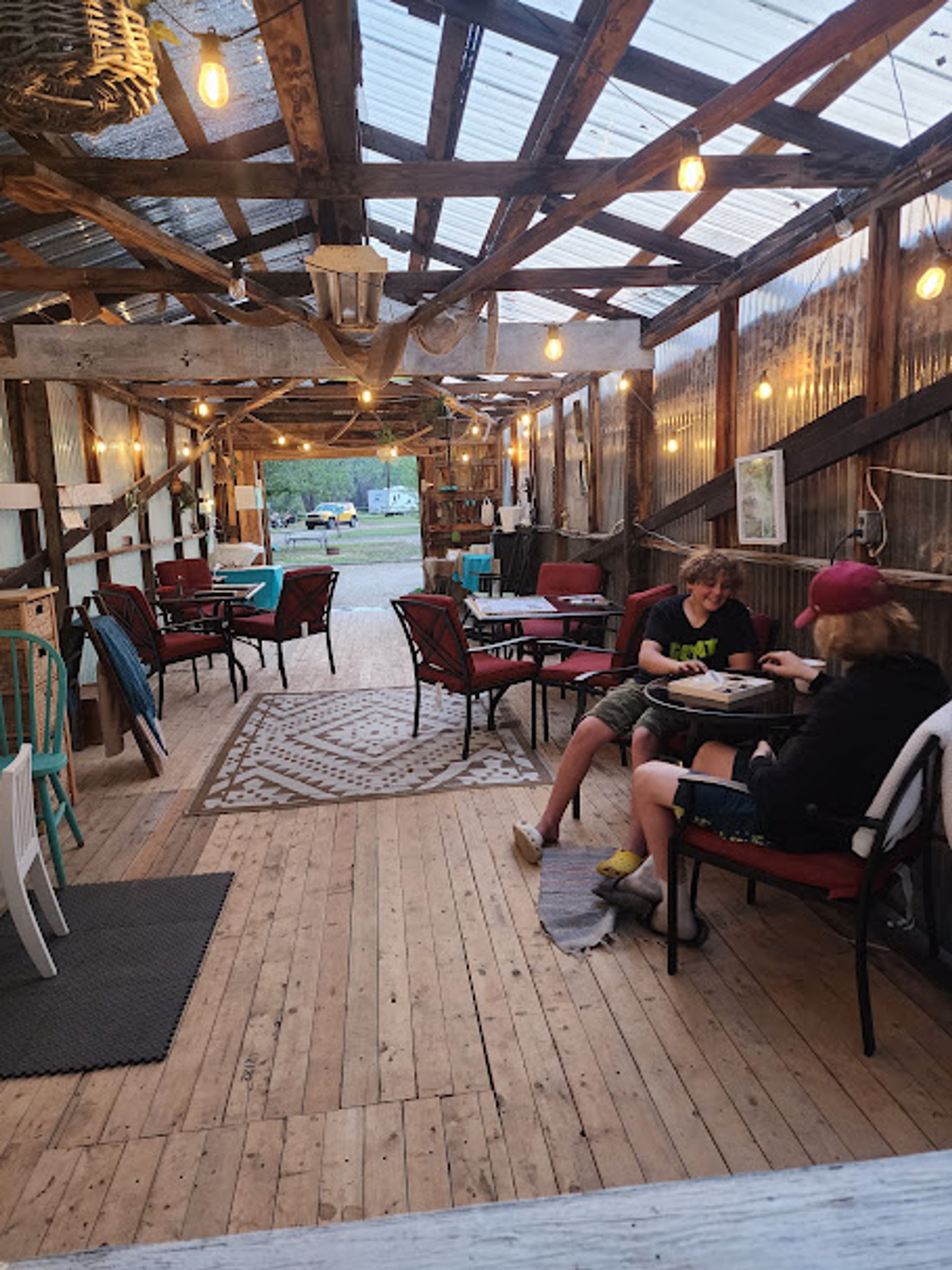 Covered patio with string lights, scattered tables and chairs, and two people eating.