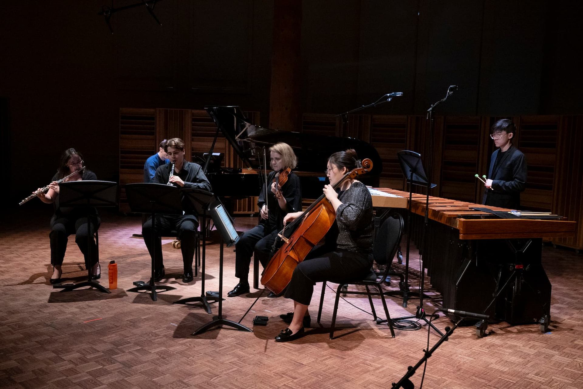 Chamber musicians perform on flute, clarinet, violin, cello, piano and marimba onstage.