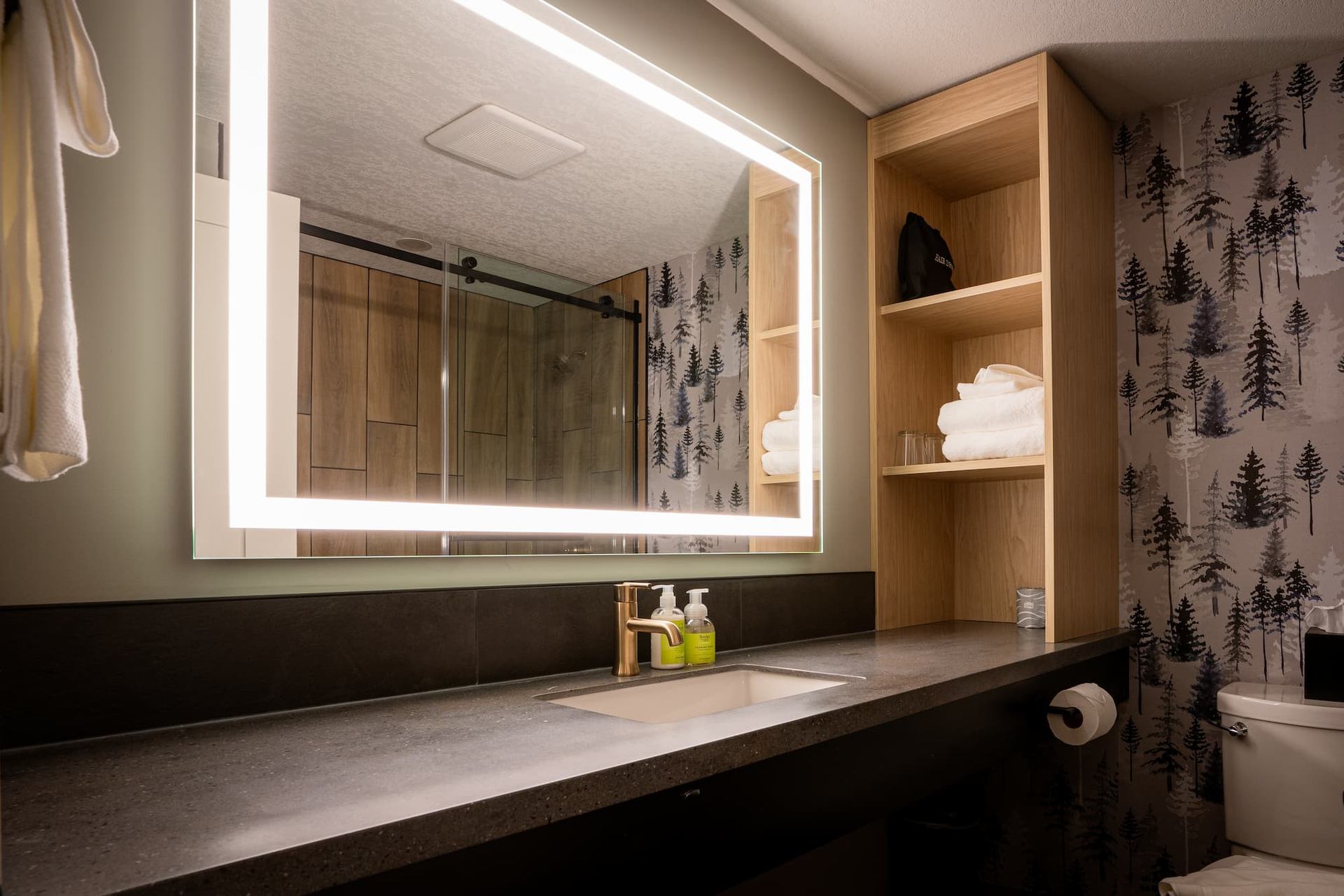 Modern bathroom with large backlit mirror and forest-patterned wallpaper at Everwild Canmore.
