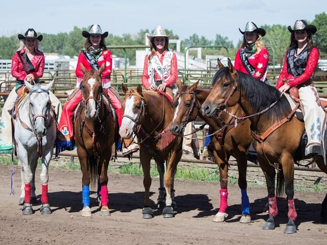 Rodeo riders in red outfits sit on decorated horses in an outdoor arena.