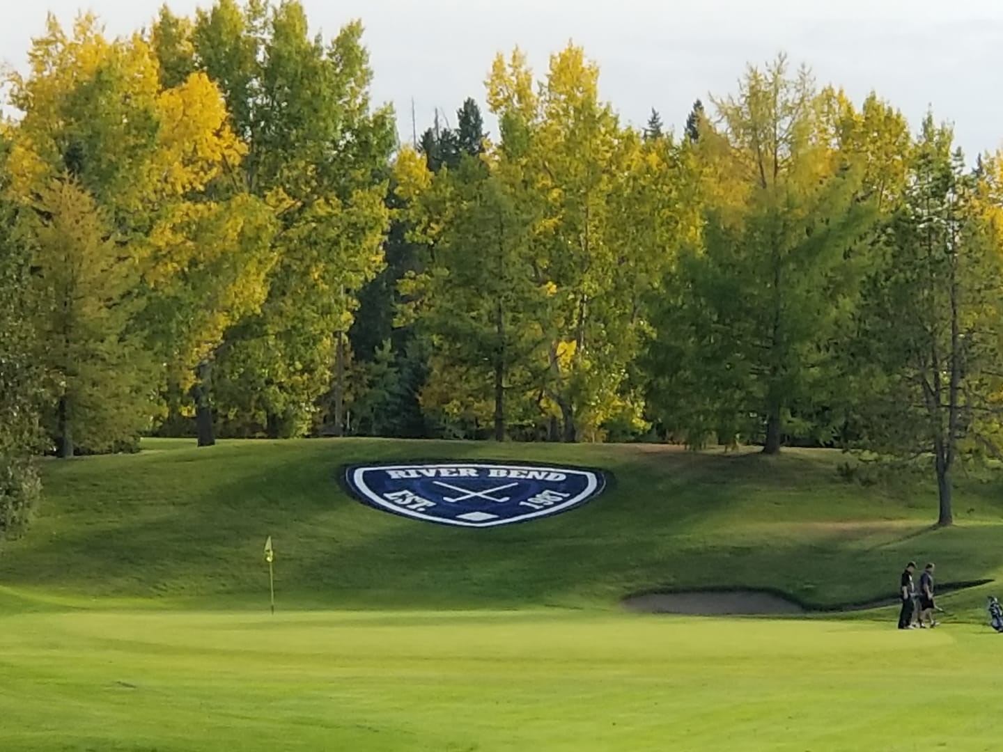 Putting green with flagstick, fall trees, and Pine Ridge emblem on hillside.