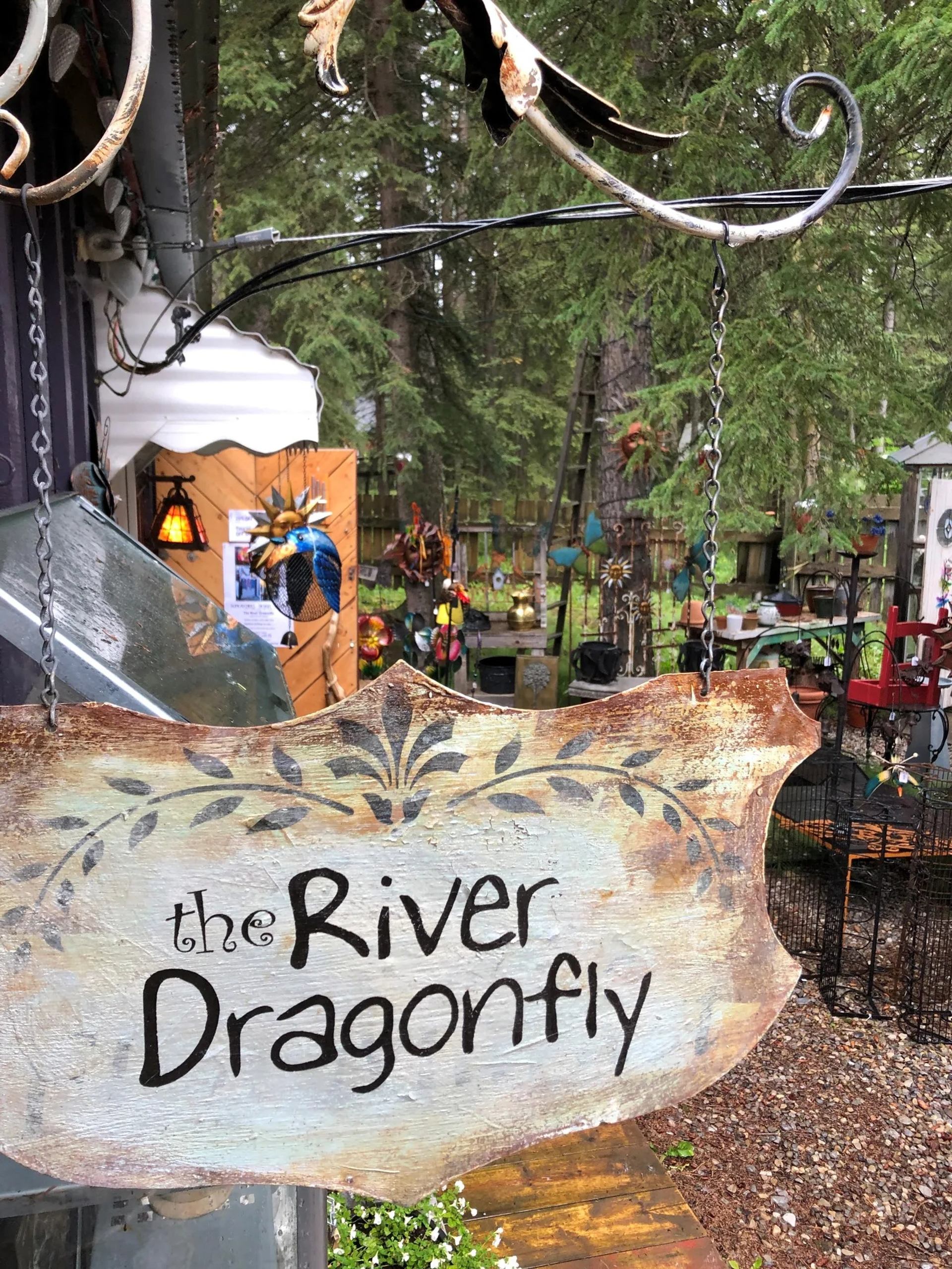 Wooden sign reading “The River Dragonfly” hanging outside a garden art shop.